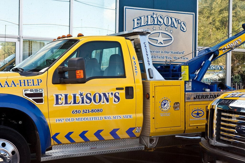 Yellow service truck with blue accents and branding for Ellison's, parked outside a building with a sign for Ellison's Auto Service.