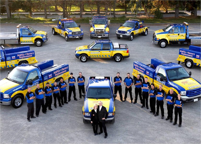 A team of emergency response vehicles and personnel, including trucks with branding for mobile fingerprint and ancestry services, arranged on a gravel lot with trees in the background.