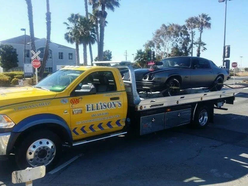 A yellow tow truck carrying a black car on its flatbed.