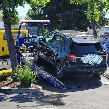 Black SUV being loaded onto a tow truck in a parking lot.