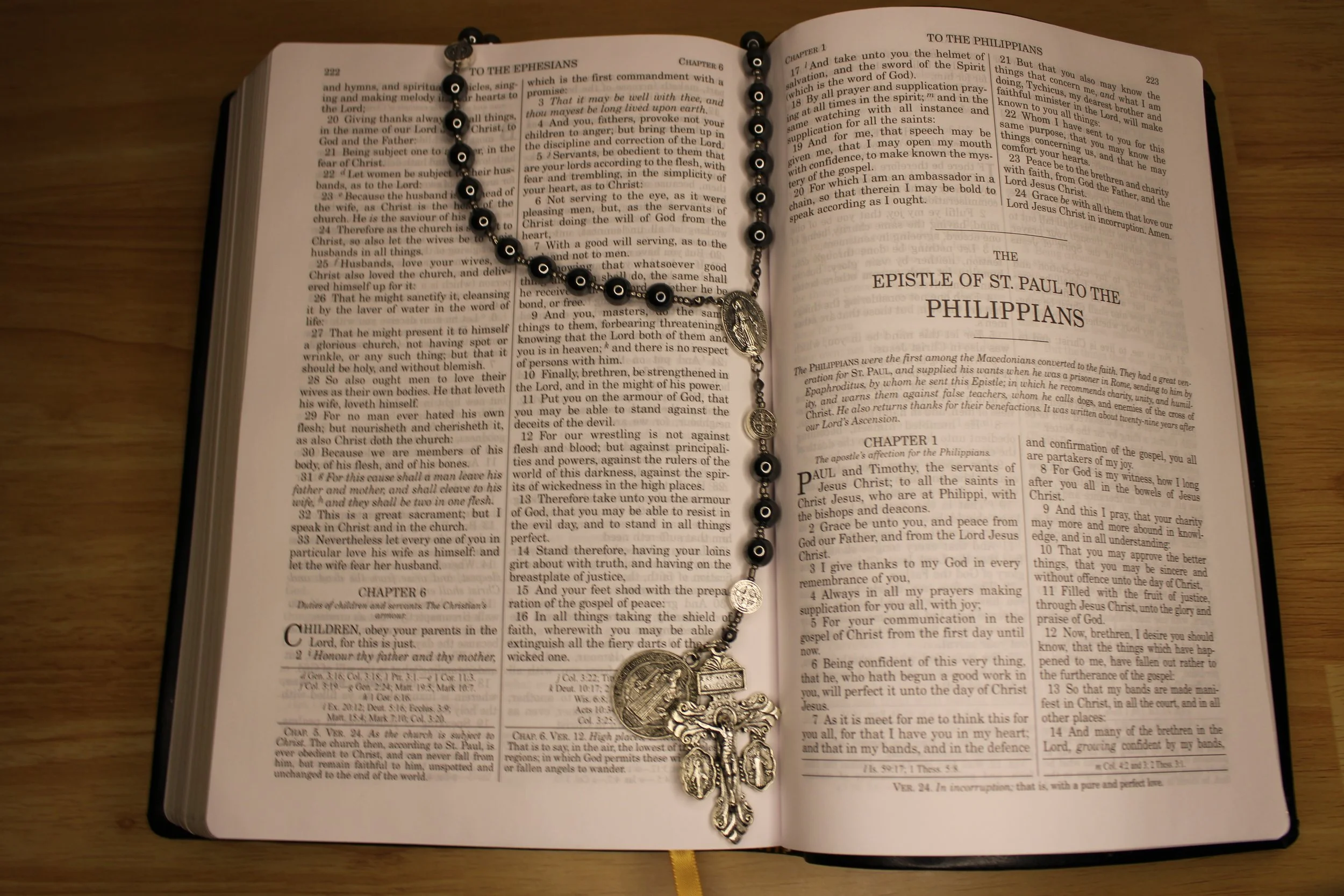 Open Bible with a rosary draped over it, resting on a wooden surface.