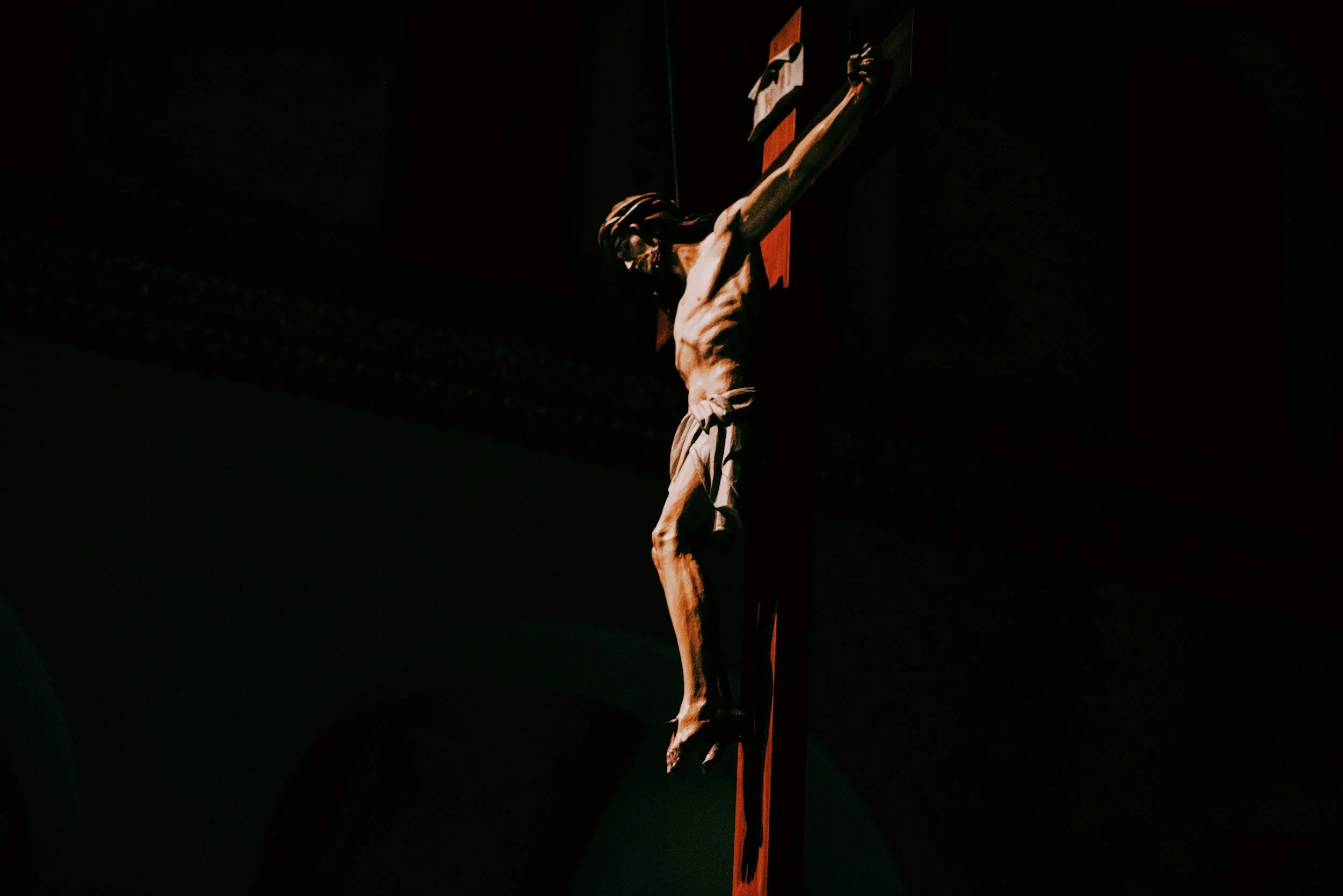 A sculpture of Jesus Christ on the cross, with a dark background and minimal lighting highlighting the figure.