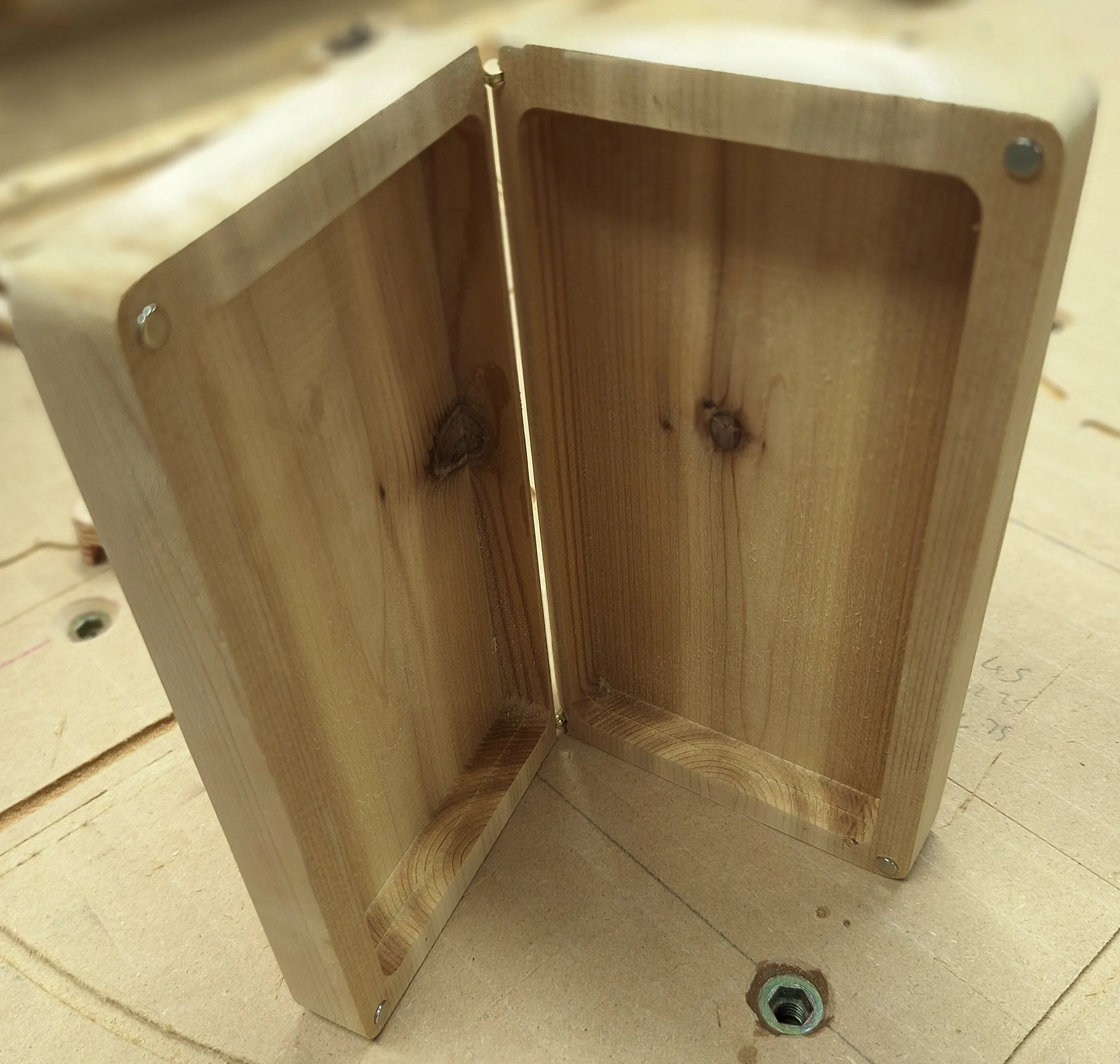 Close-up of a piece of unfinished wooden furniture, possibly a cabinet or shelf, with visible screws and hardware, sitting on a wood surface.