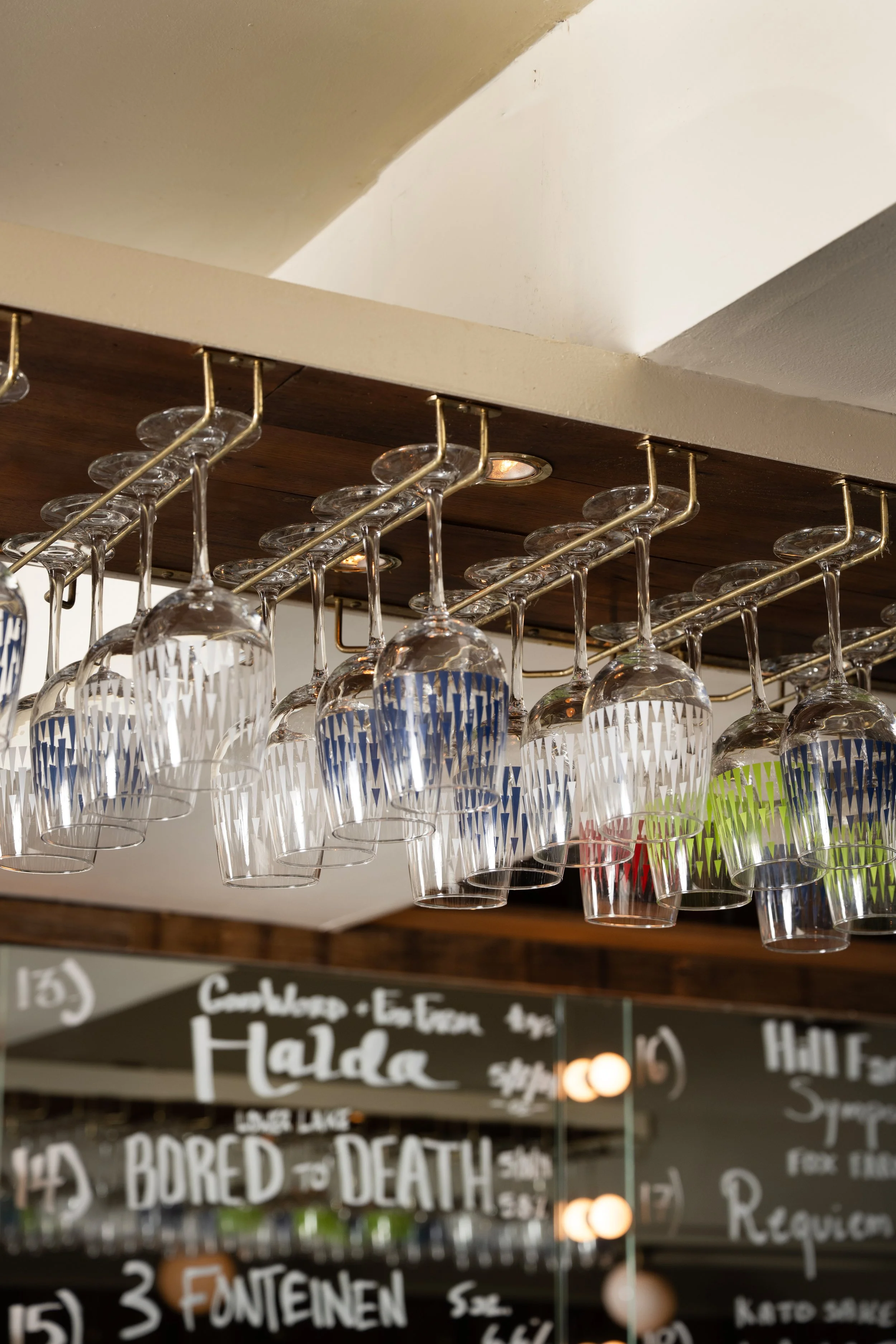 Tørst patterned glassware hanging from brass overhead rack with handwritten draft list visible below