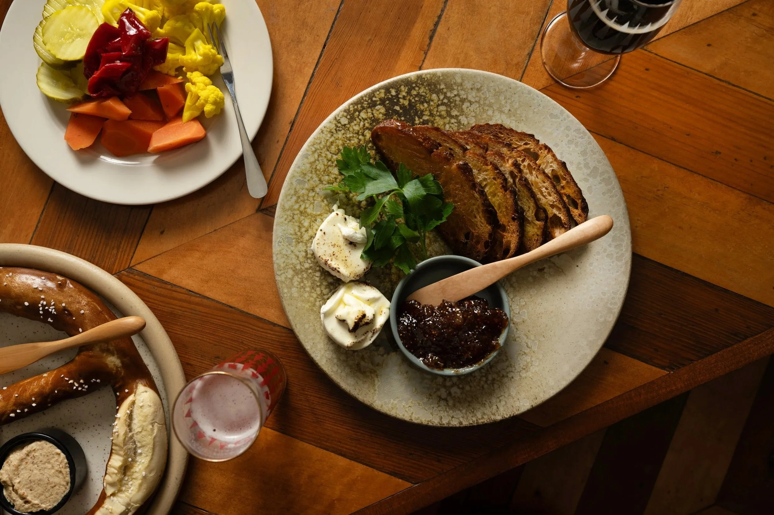 Overhead table spread at Tørst featuring cheese plate, pickled vegetables, and a pretzel alongside beer and patterned glassware