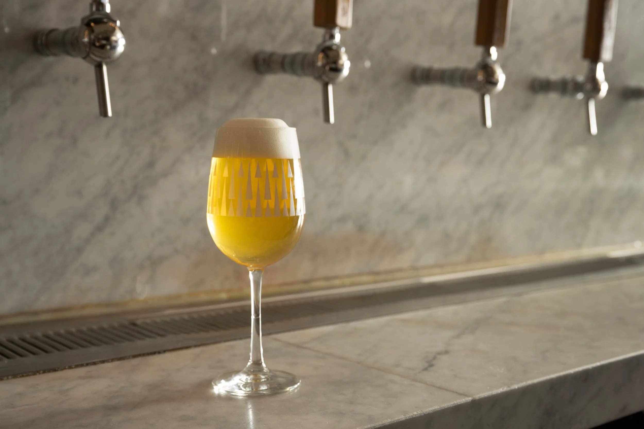 Patterned Tørst beer glass filled with golden draft beer sitting in front of multiple tap handles on the marble bar