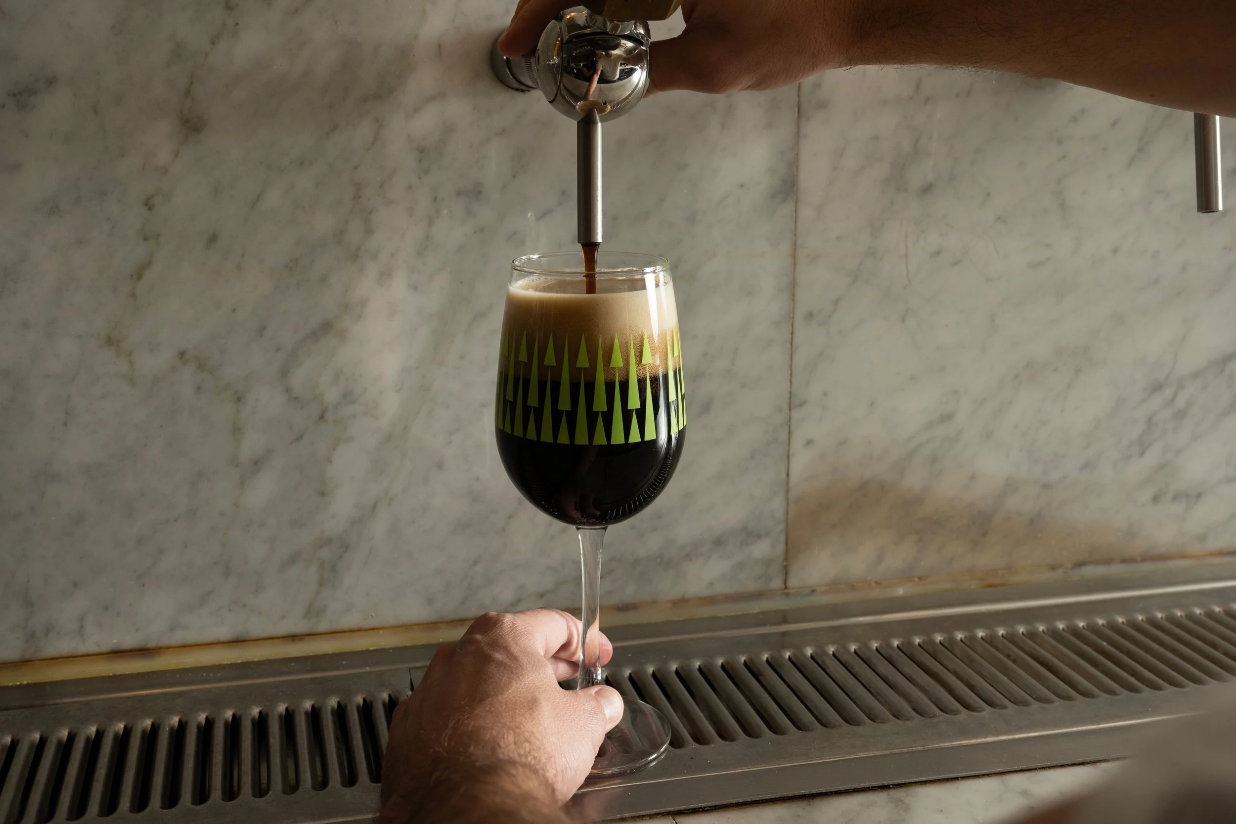 Dark stout being poured from a draft tap into a green patterned Tørst glass against a marble bar back