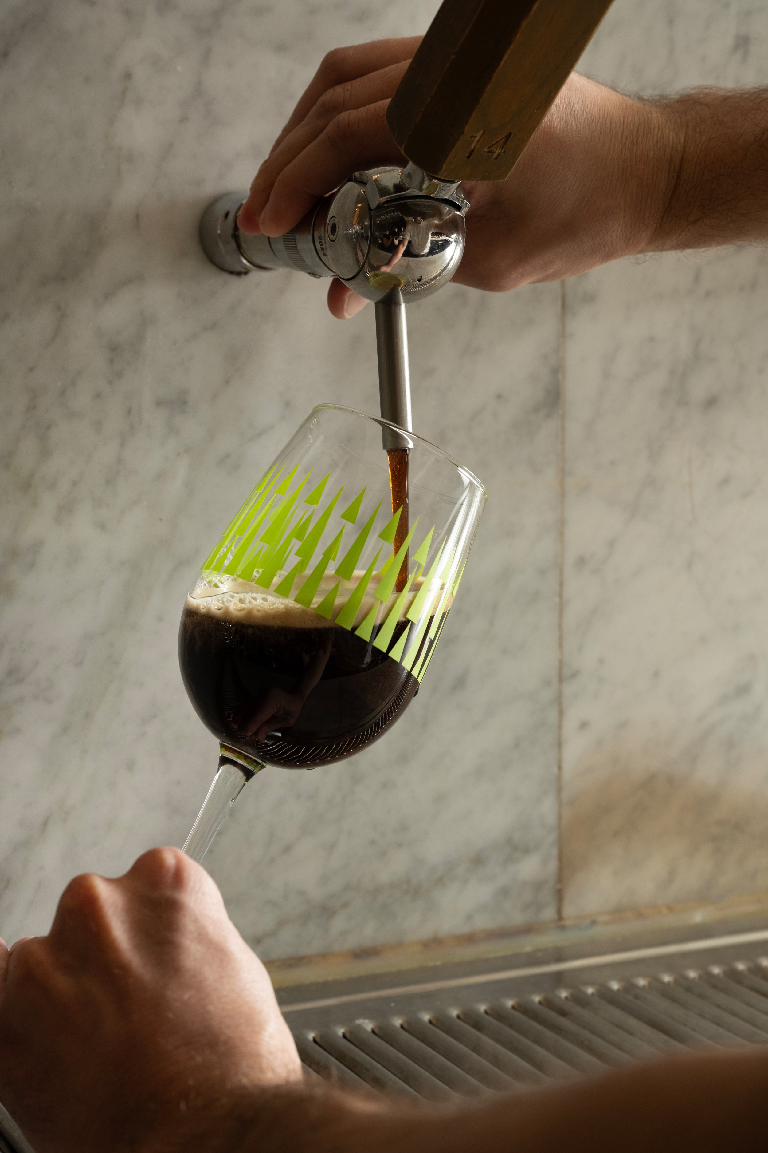 Dark beer being poured from tap 14 into a green patterned Tørst glass against a marble bar back