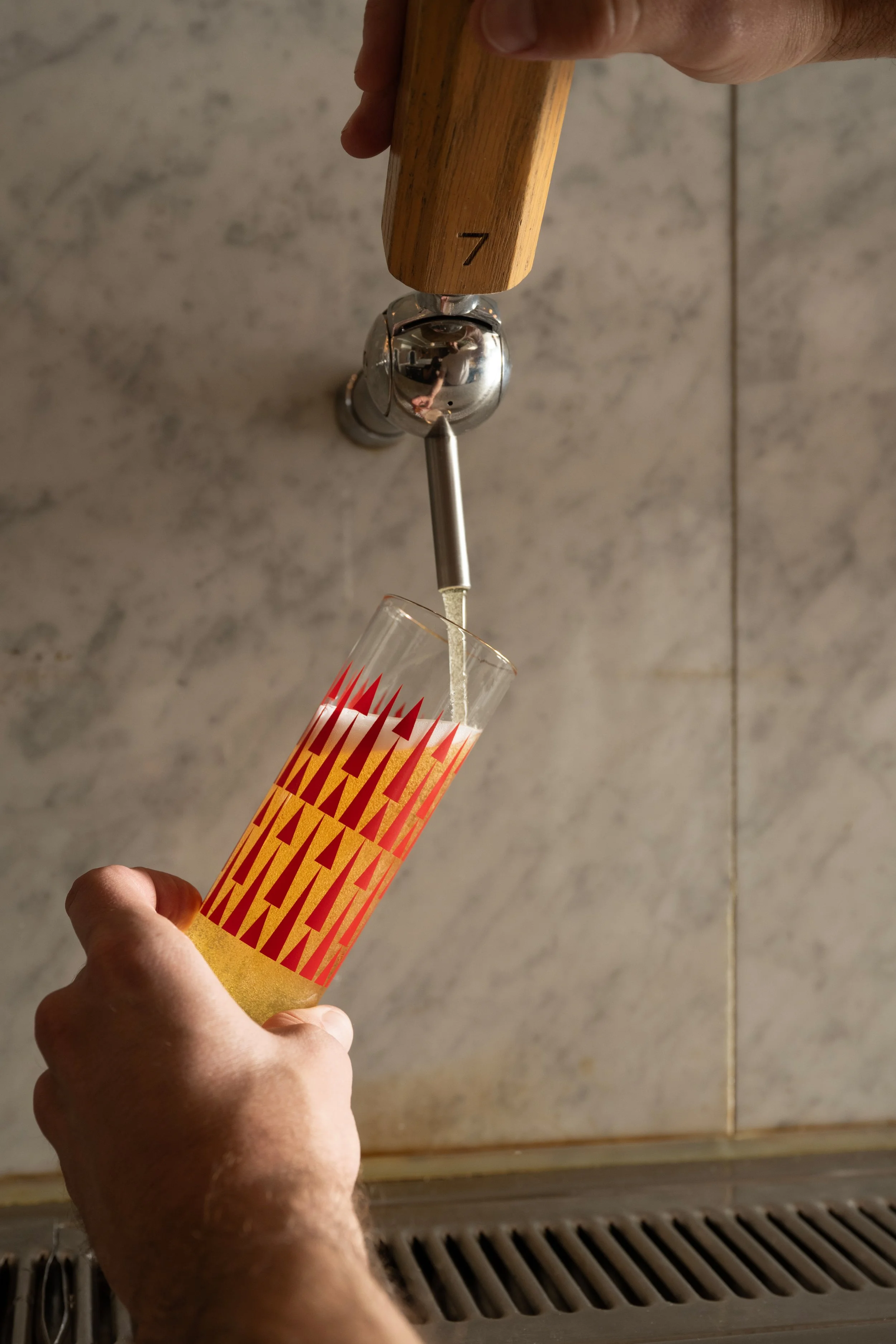 Golden beer being poured from tap 7 into a red patterned Tørst pilsner glass against a marble bar back