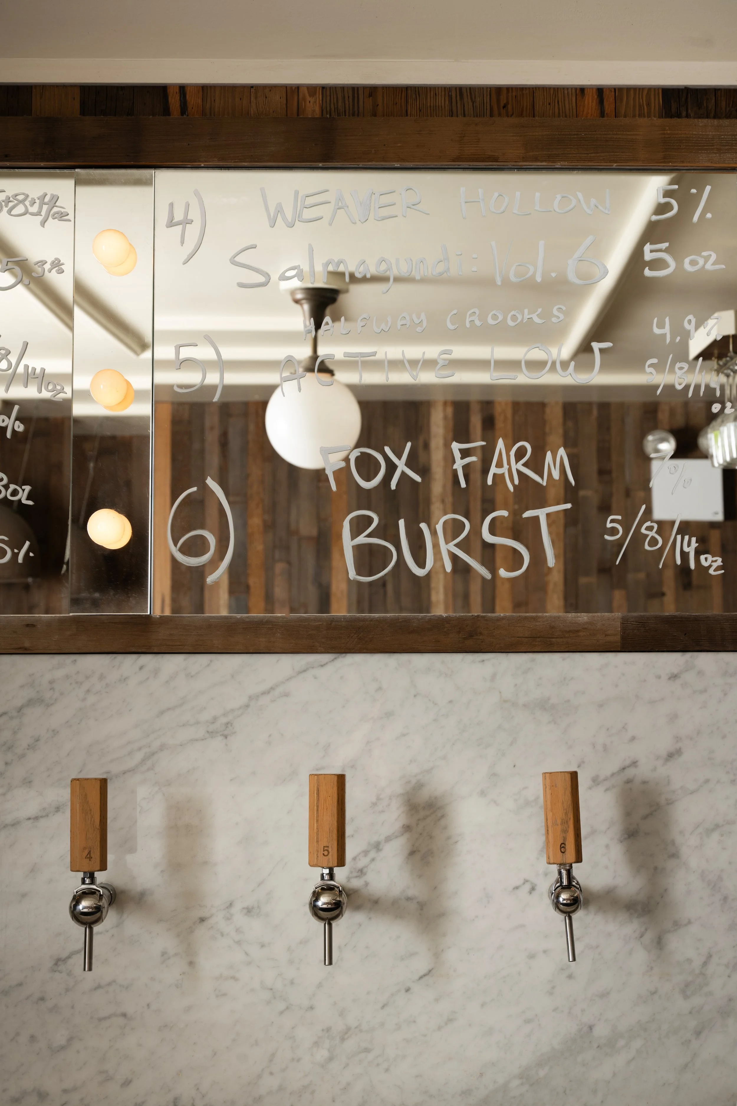 Detail of Tørst's handwritten draft beer menu on the mirrored bar back, featuring tap handles and hanging glassware