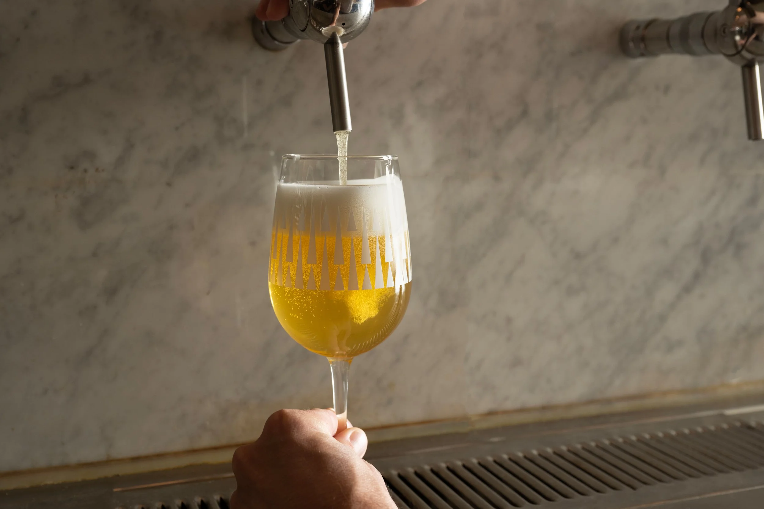 Golden draft beer being poured from tap into a patterned Tørst glass against a marble bar back