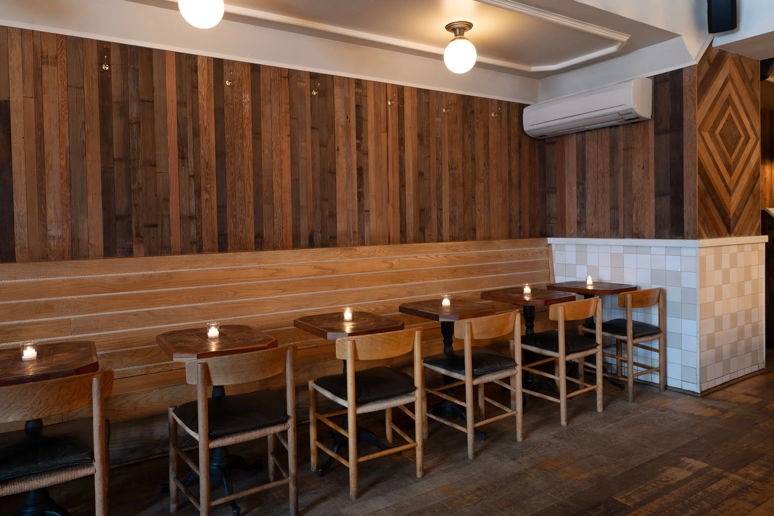 Tørst dining room seating area with wood banquette, small tables, globe lights, and the private back room visible in the background