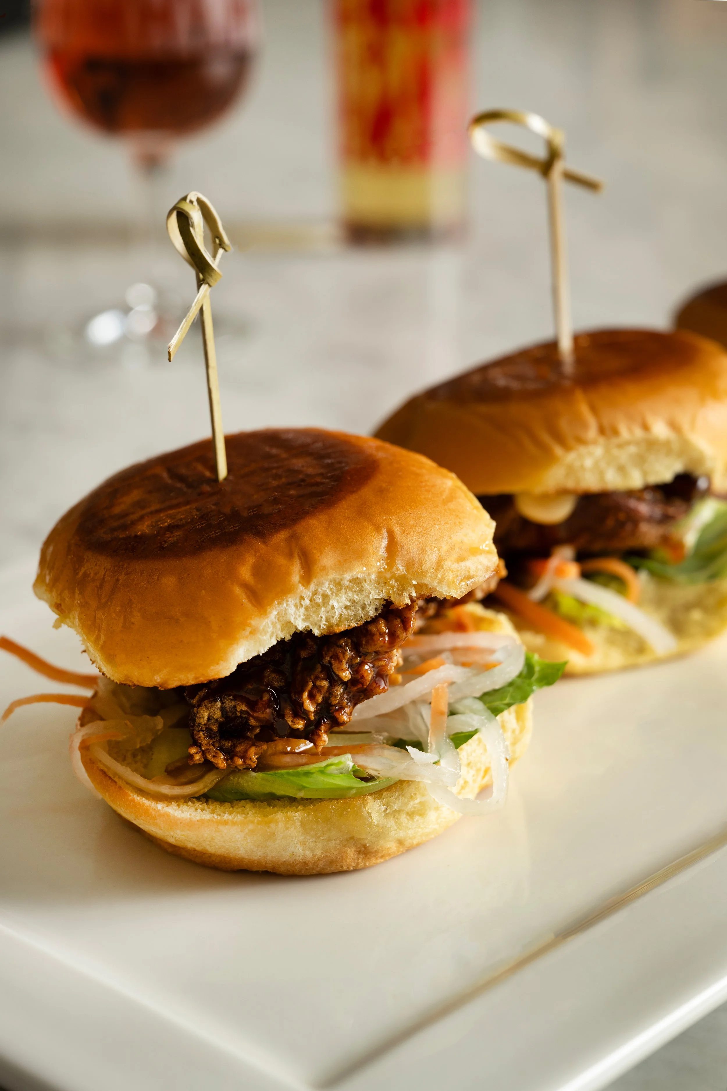 Three fried chicken sandwich sliders with chili miso honey glaze, pickled carrot and daikon, and garlic aioli on potato buns, served on a marble board