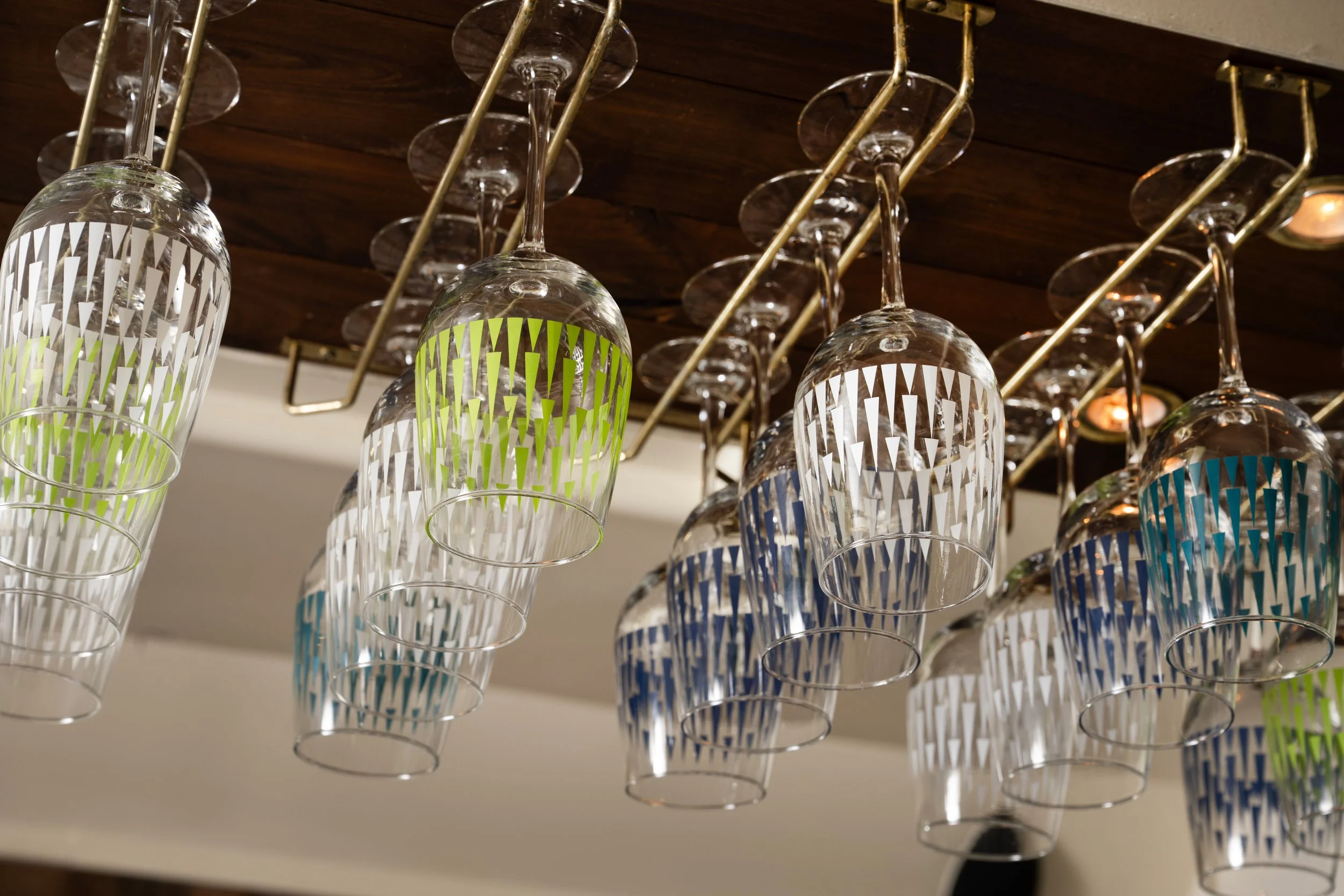 Colorful patterned beer glasses hanging upside down from brass rack above Tørst's bar