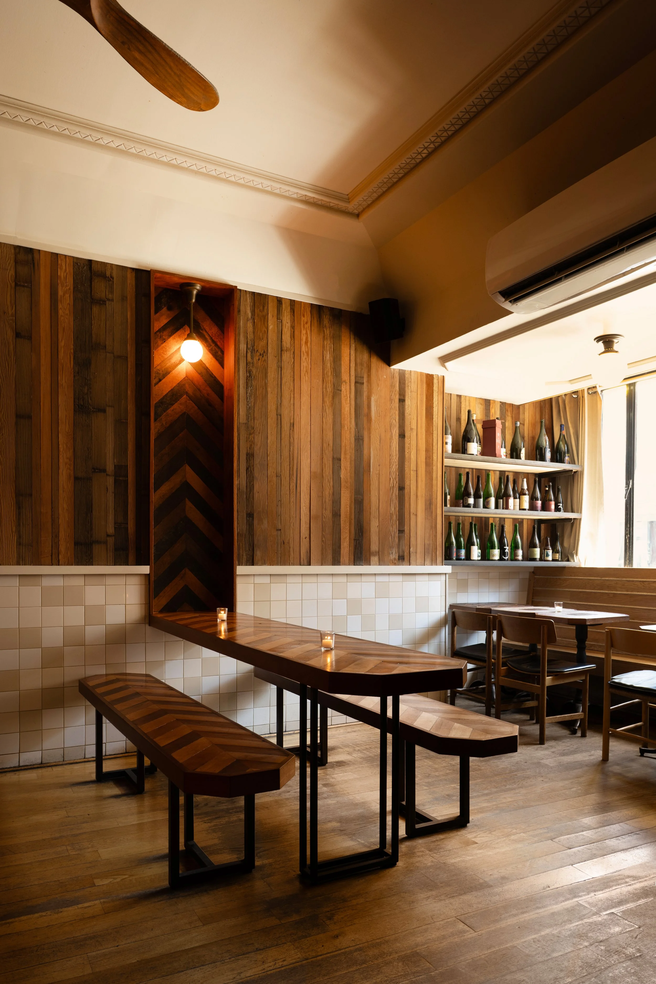 Corner of Tørst's dining room featuring herringbone wood accent walls, a bottle shelf display, and warm overhead lighting