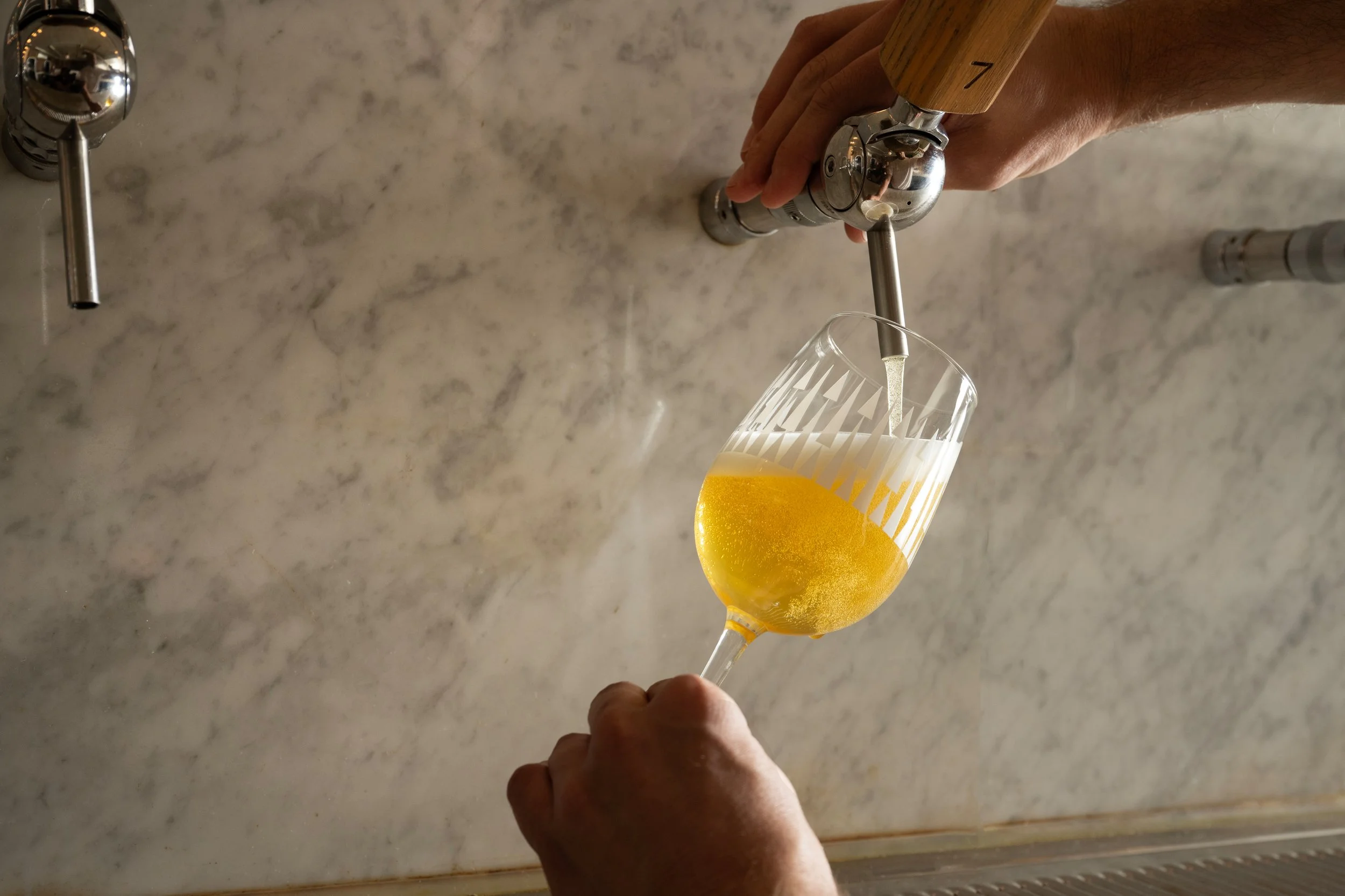 Close-up of a golden beer being poured from tap 7 into a tilted patterned Tørst glass at the marble bar