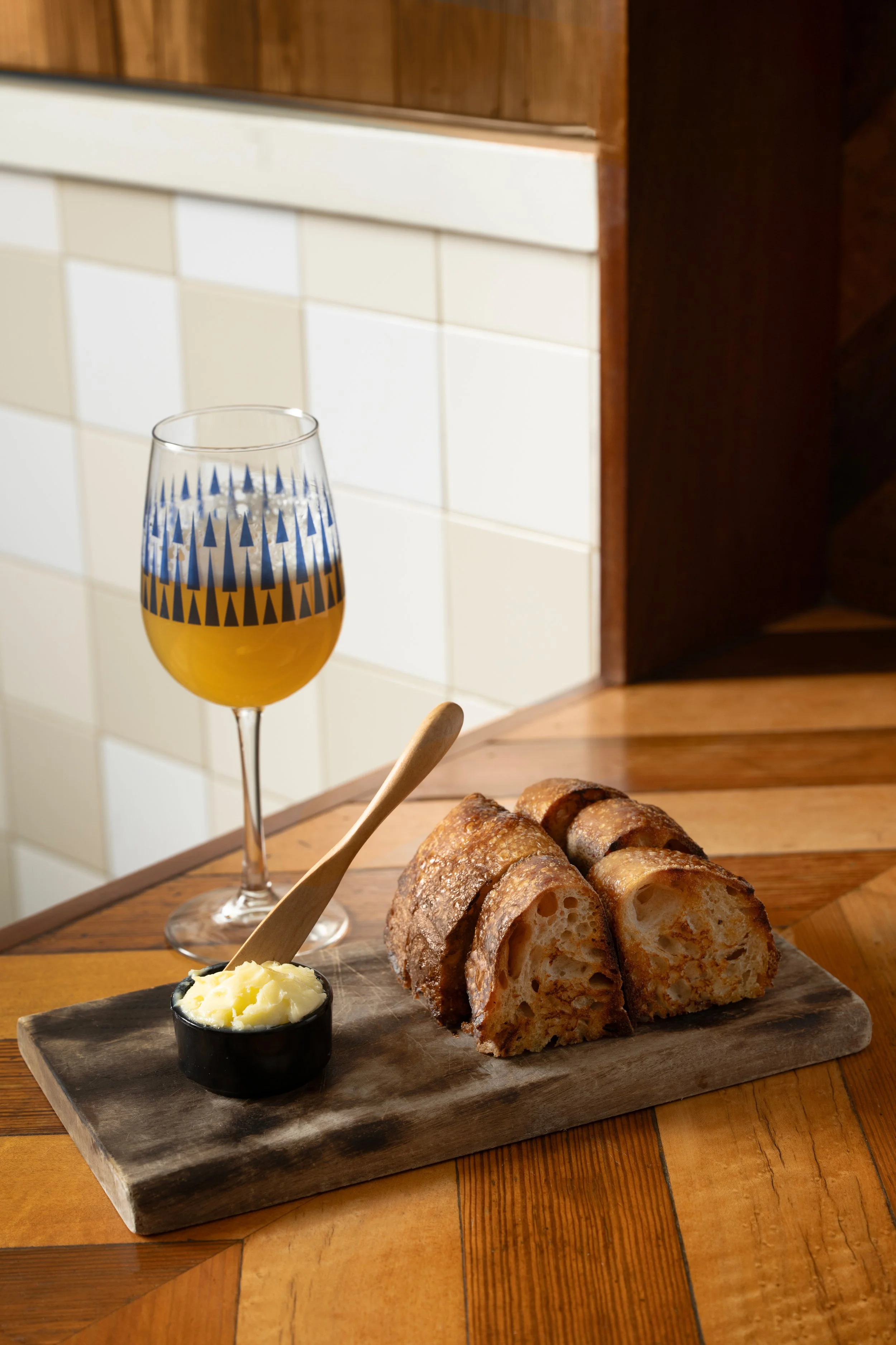 She-Wolf sourdough bread sliced and served on a wooden board with house cultured butter and a patterned Tørst beer glass