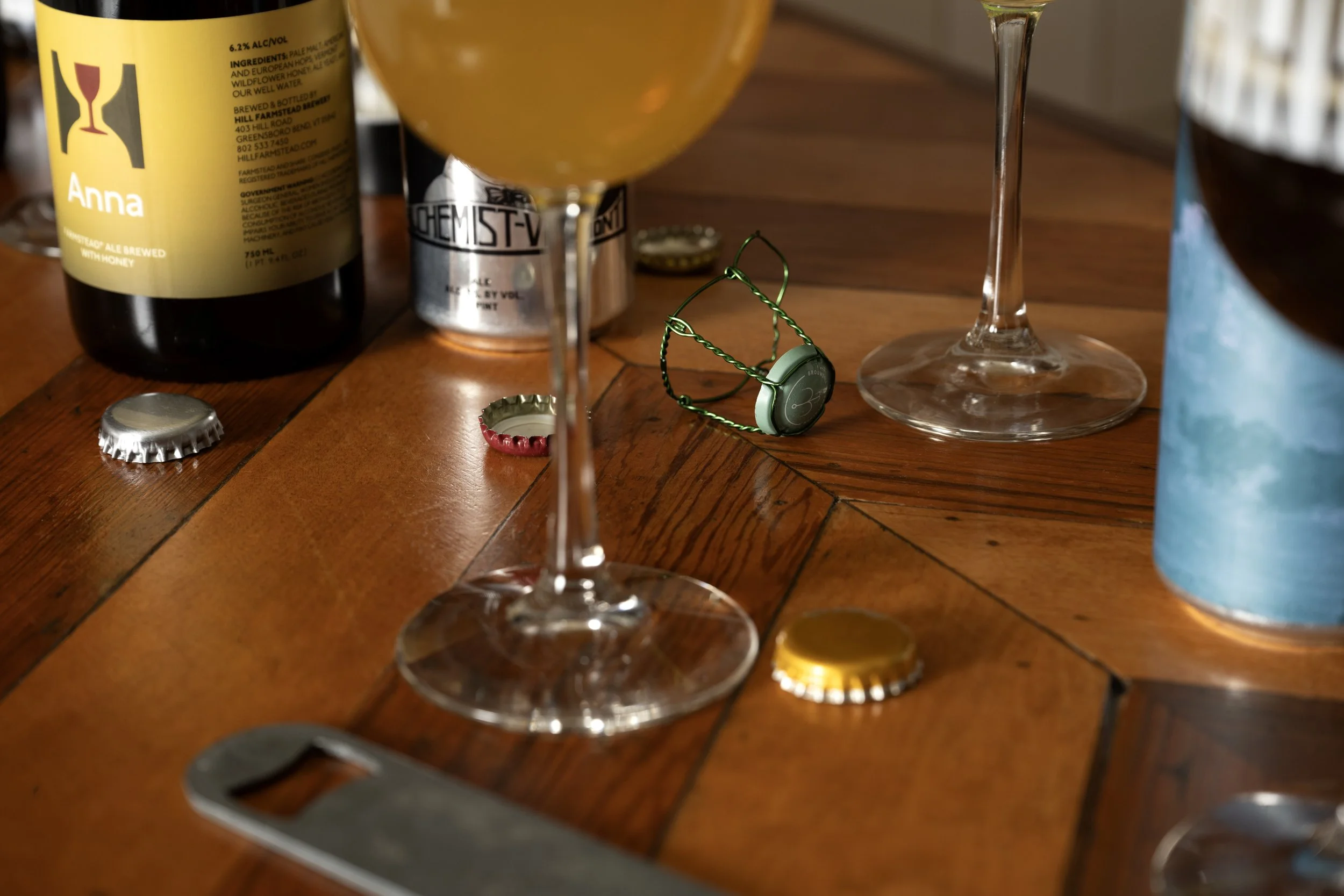 Close-up of beer bottle and beer can alongside patterned Tørst glasses, bottle caps, and a bottle opener on a herringbone wood table
