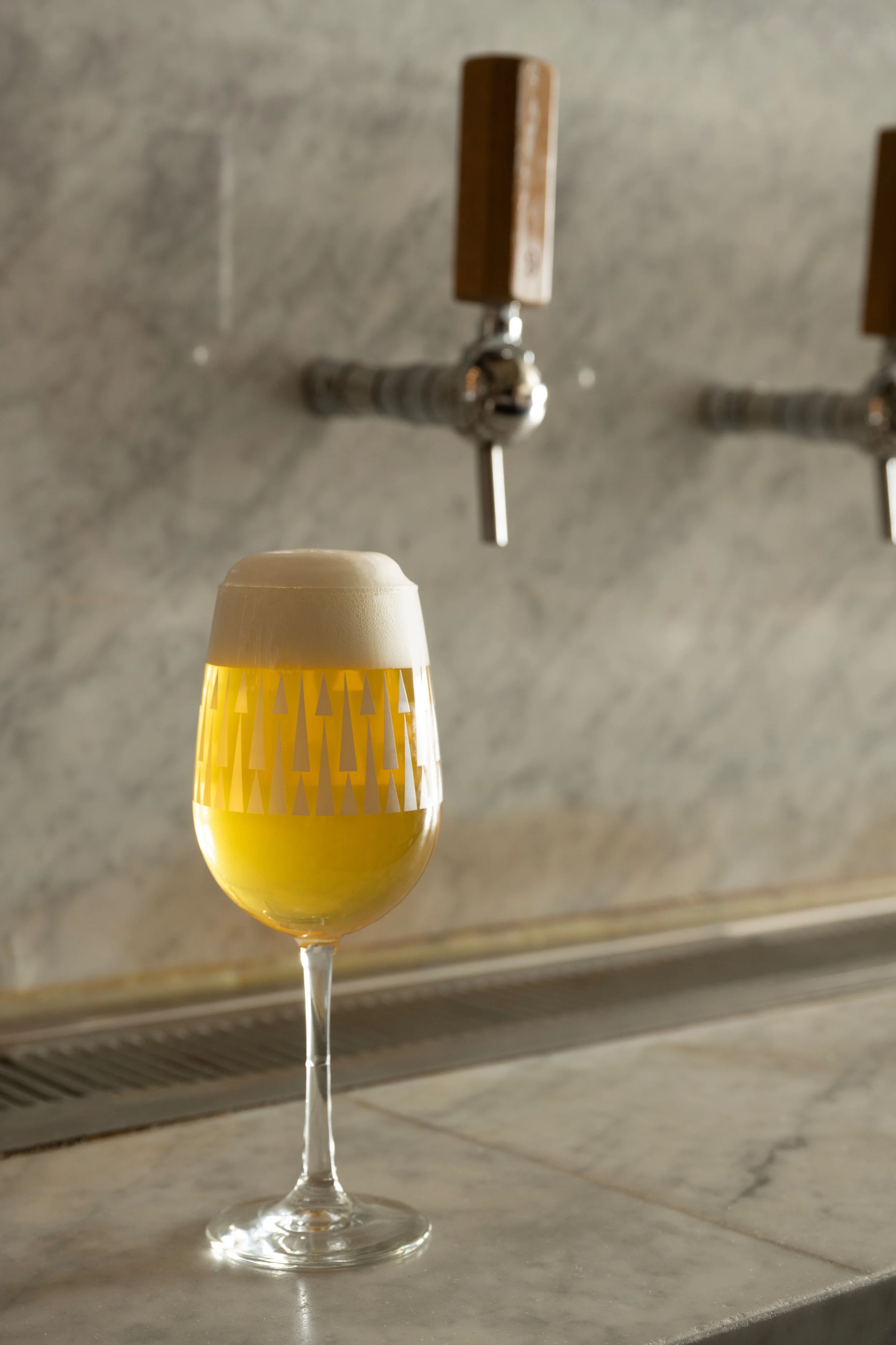 Freshly poured golden beer in a patterned Tørst glass resting on the marble bar with wooden draft tap handles in the background
