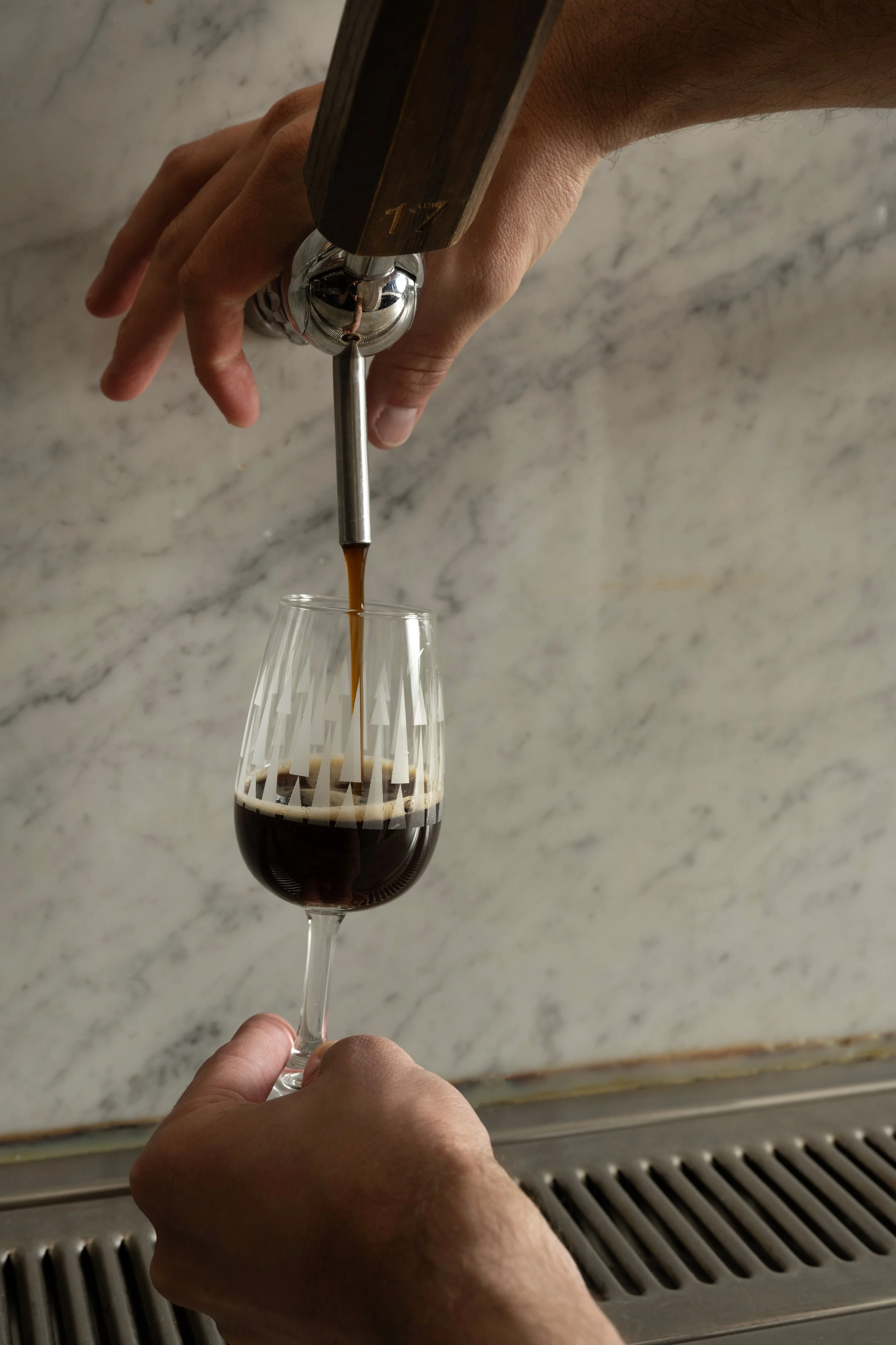 Dark beer being poured from tap 17 into a clear patterned Tørst glass against a marble bar back