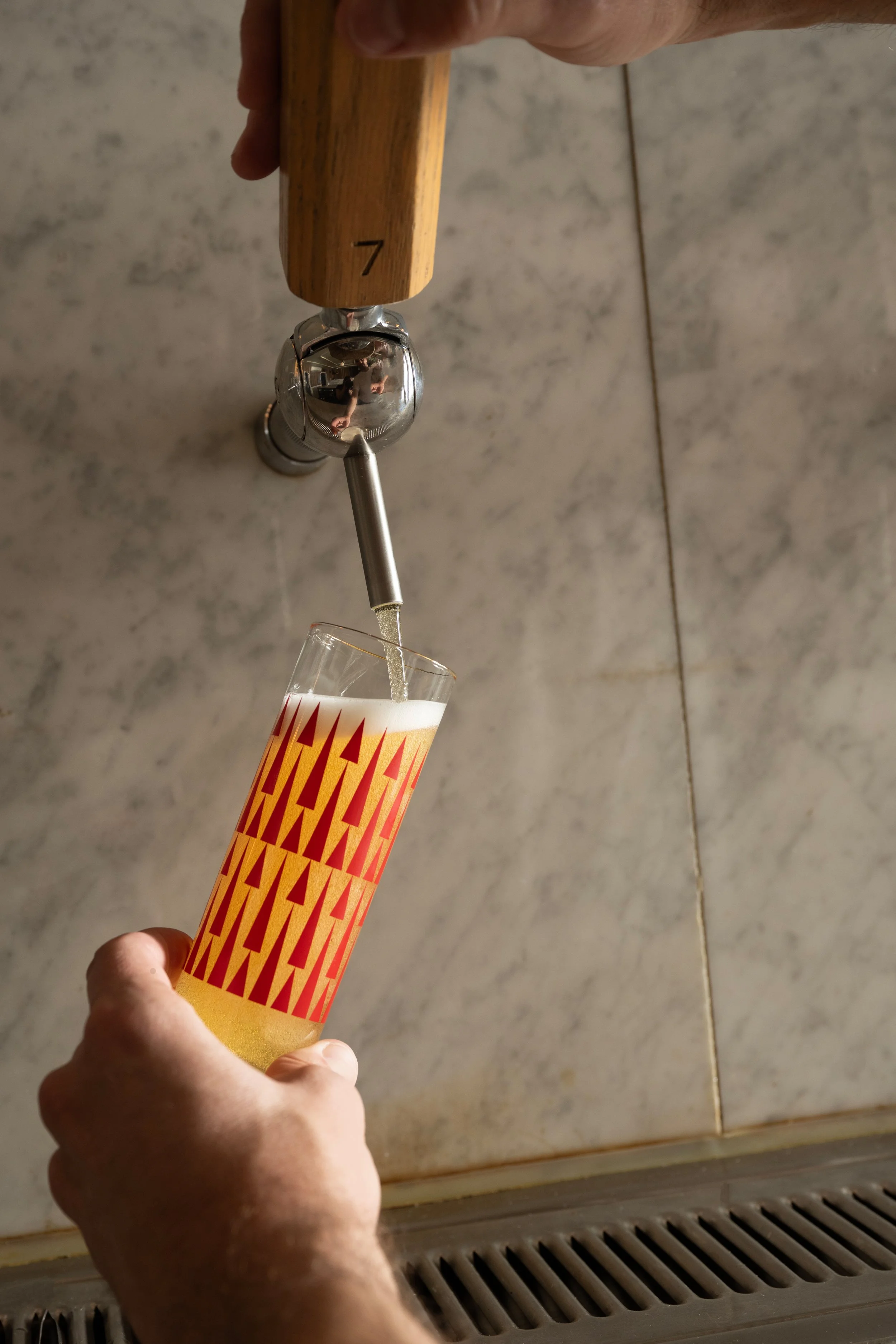 Beer being poured from tap 7 into a red patterned Tørst pilsner glass against a marble bar back