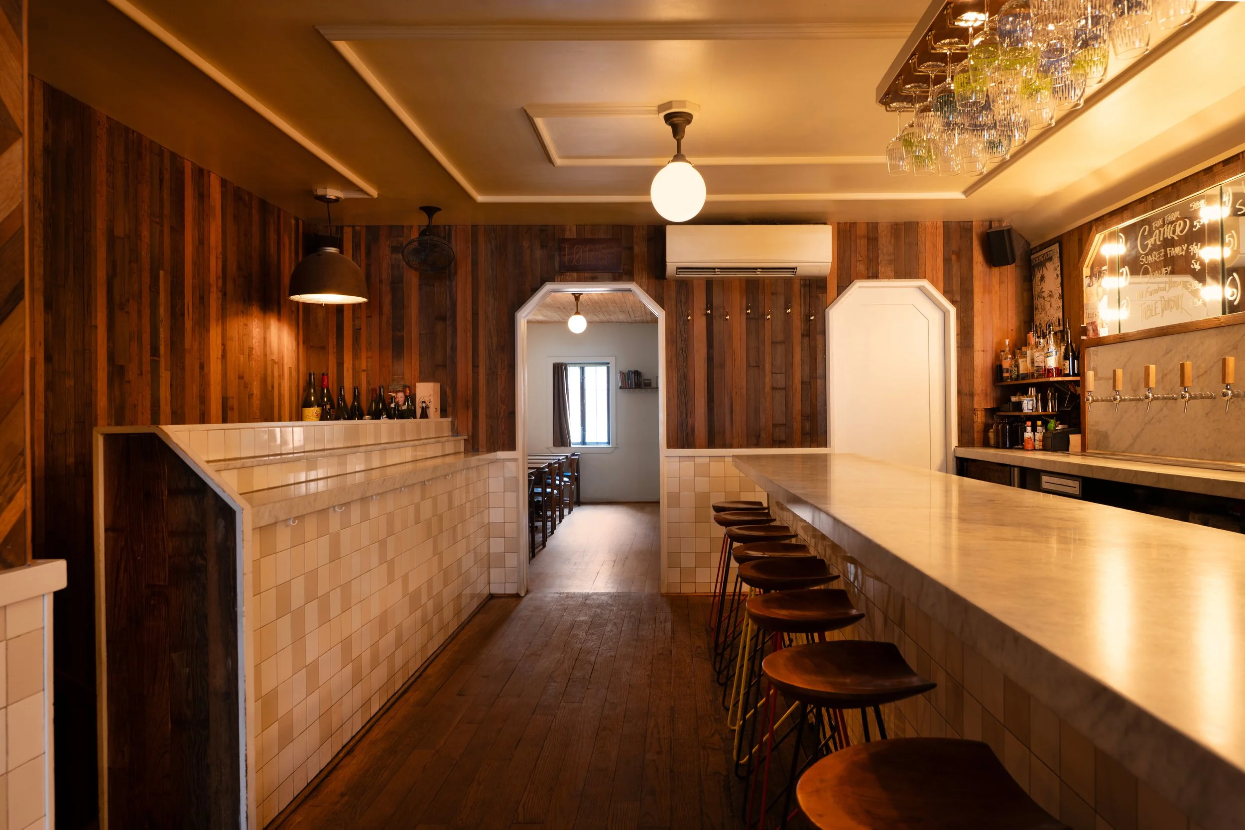 Warm interior view of Tørst's front bar area with tap handles, hanging glassware, and the back room visible through an archway