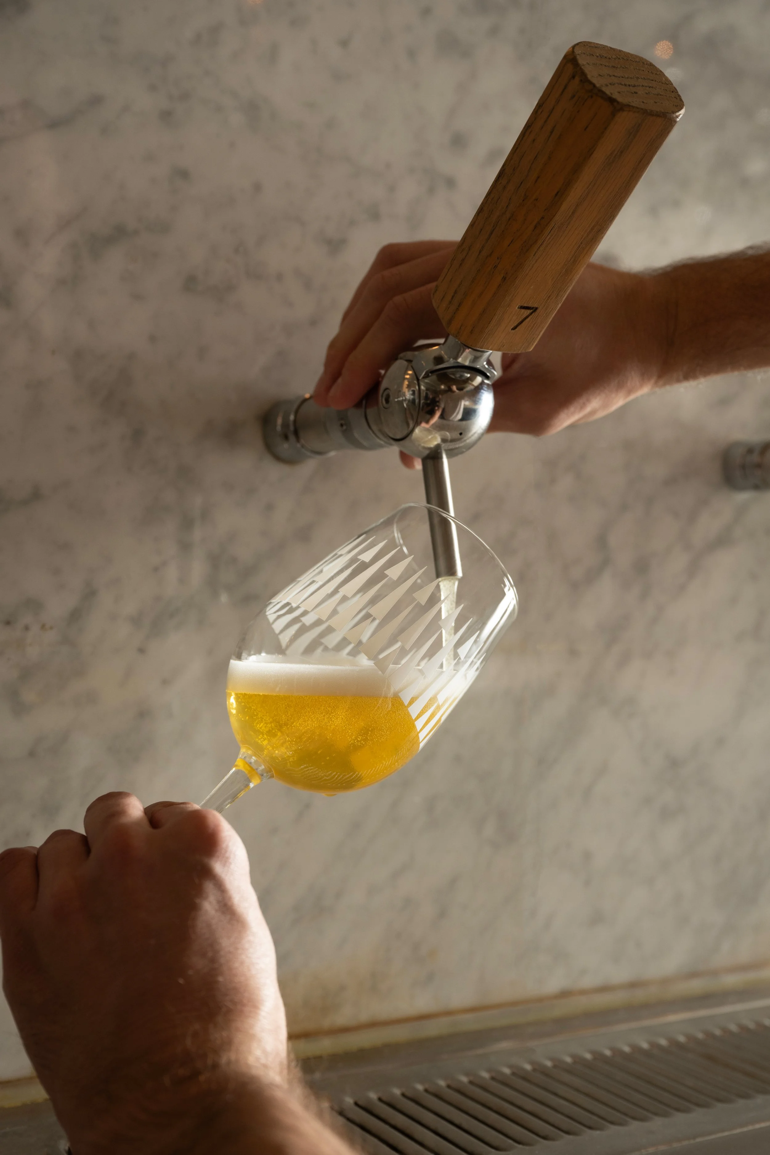 Bartender pouring a golden beer from tap 7 into an angled patterned Tørst glass against a marble bar back