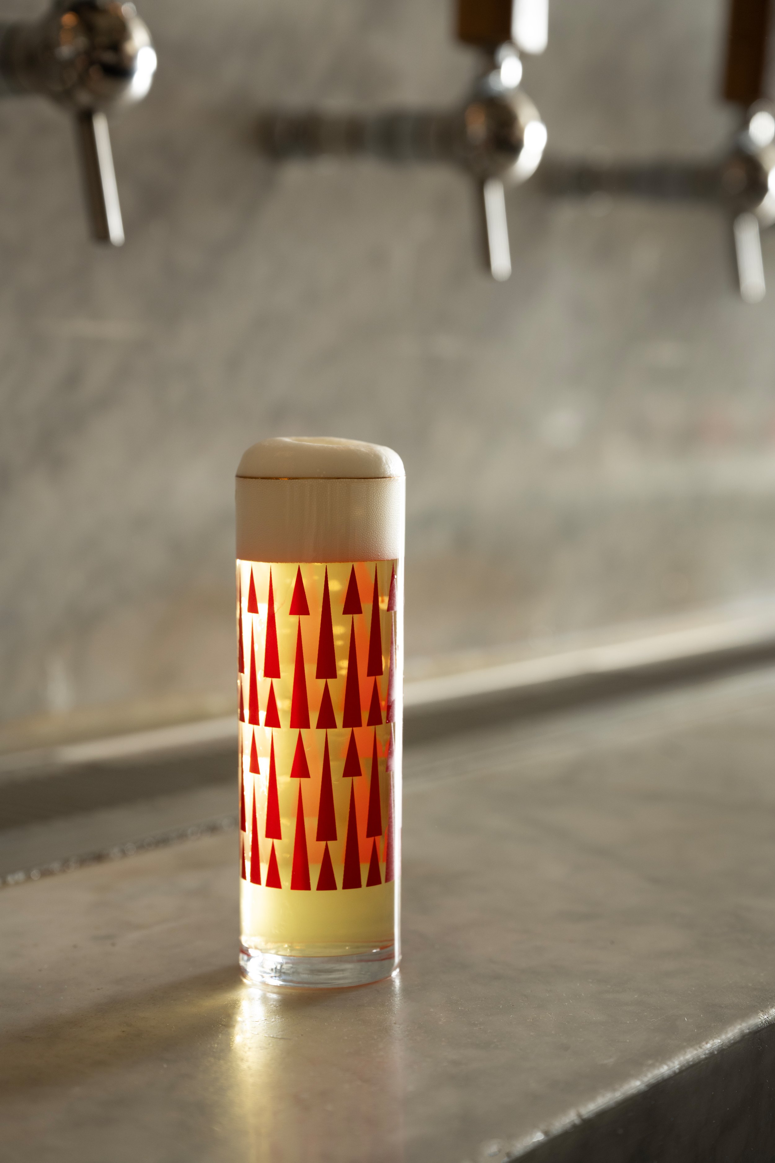 Red patterned Tørst beer glass with a perfect head of foam resting on the marble bar with two wooden draft tap handles in the background