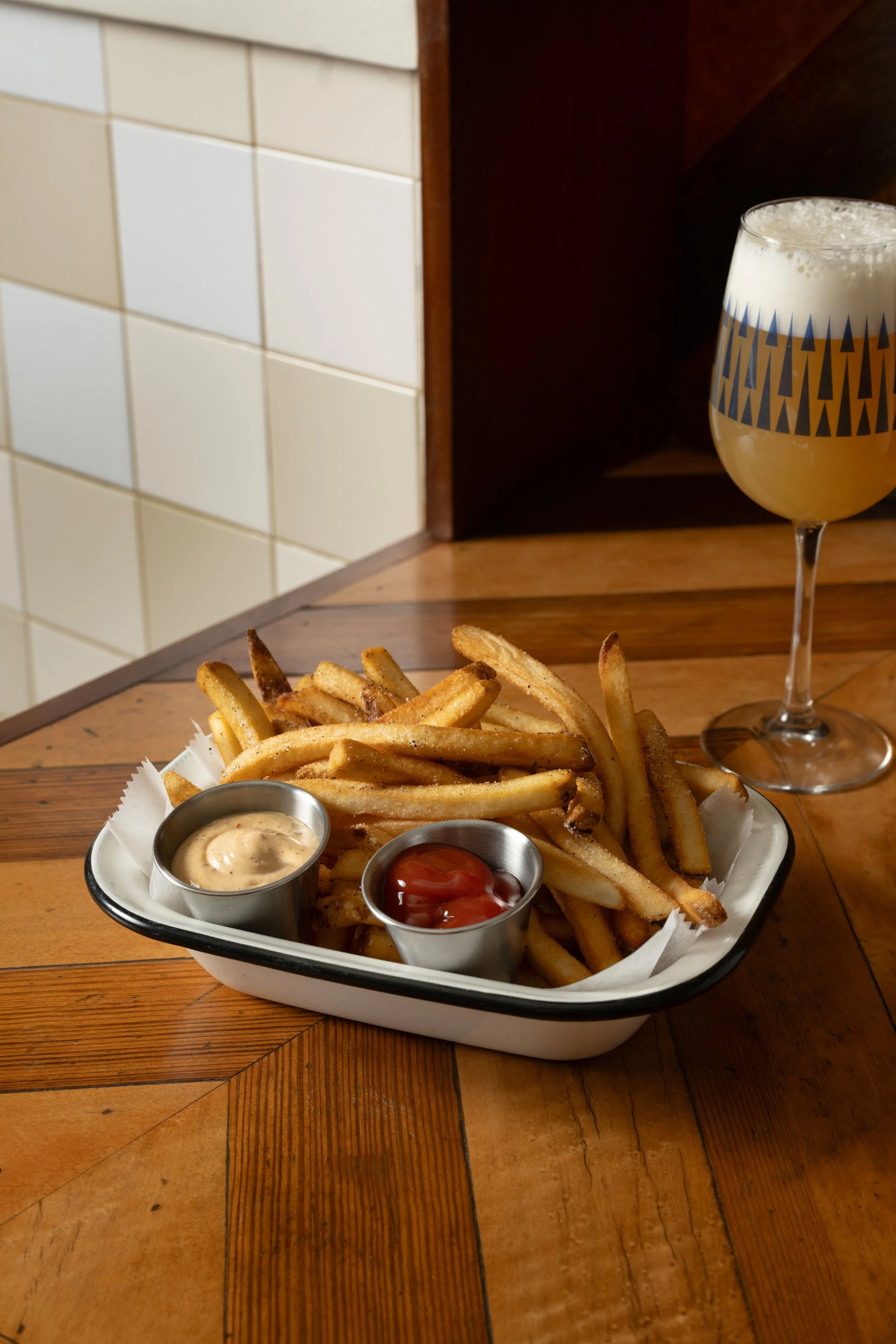 Kennebec fries in an enamel tray with chili mayo and ketchup dipping sauces, served alongside a patterned Tørst beer glass