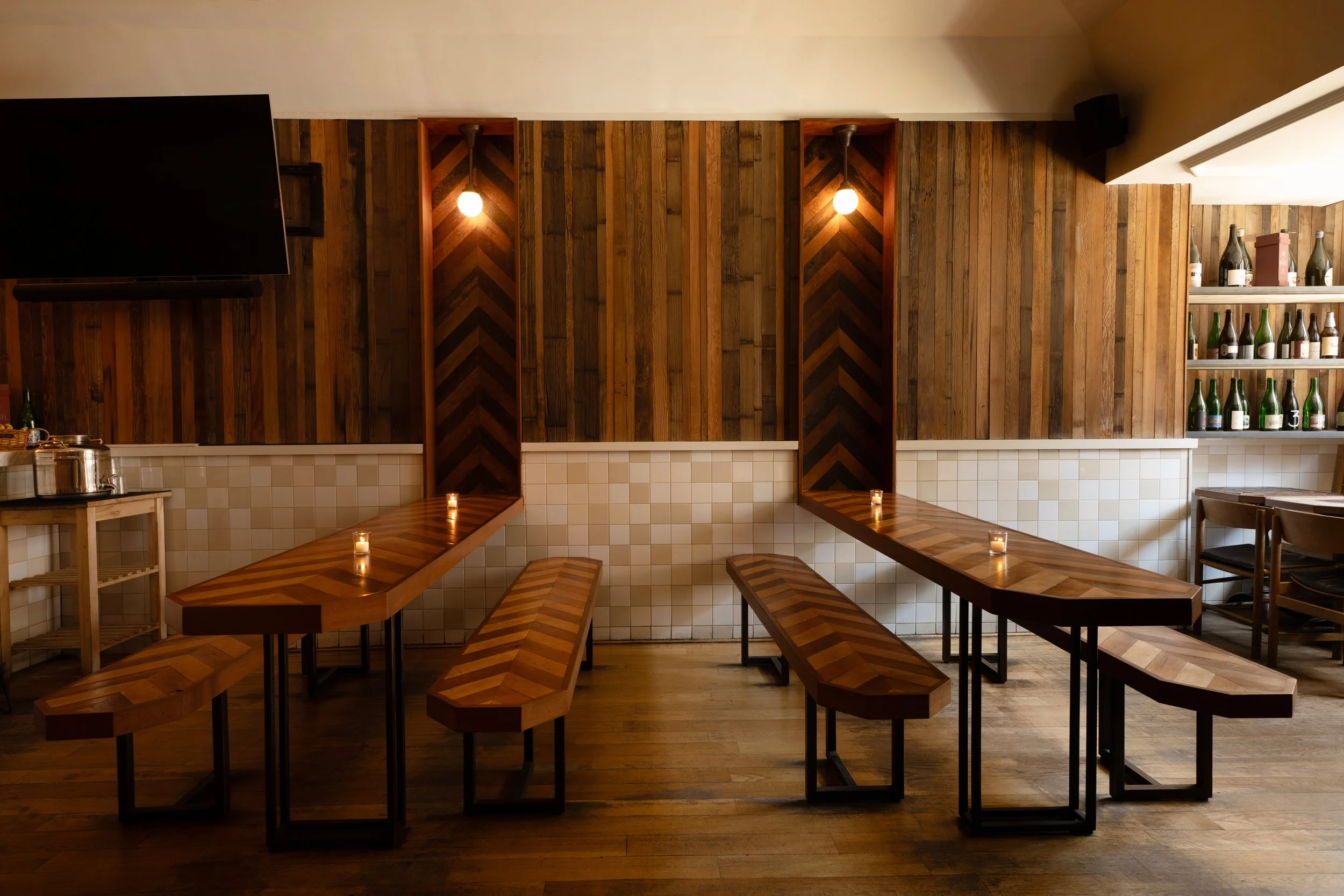 Empty back dining room at Tørst with herringbone wood paneling, communal bench tables, and candlelight