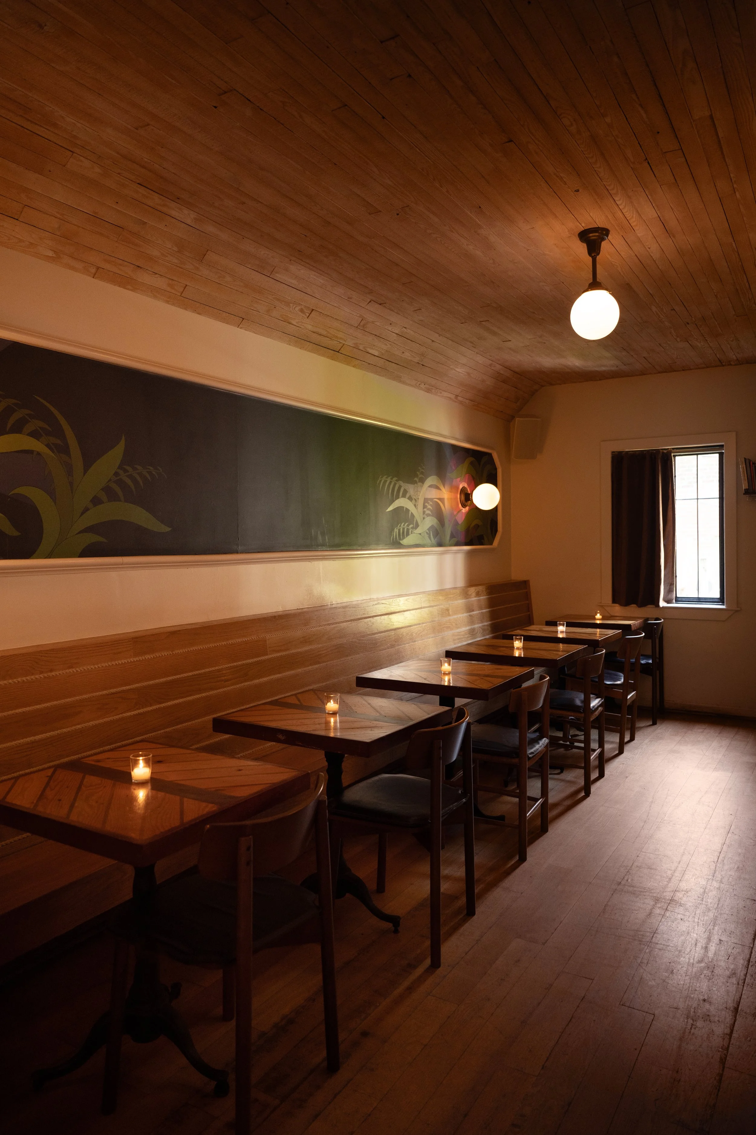 Intimate back dining room at Tørst with wood ceiling, mural, and candlelit tables in warm light