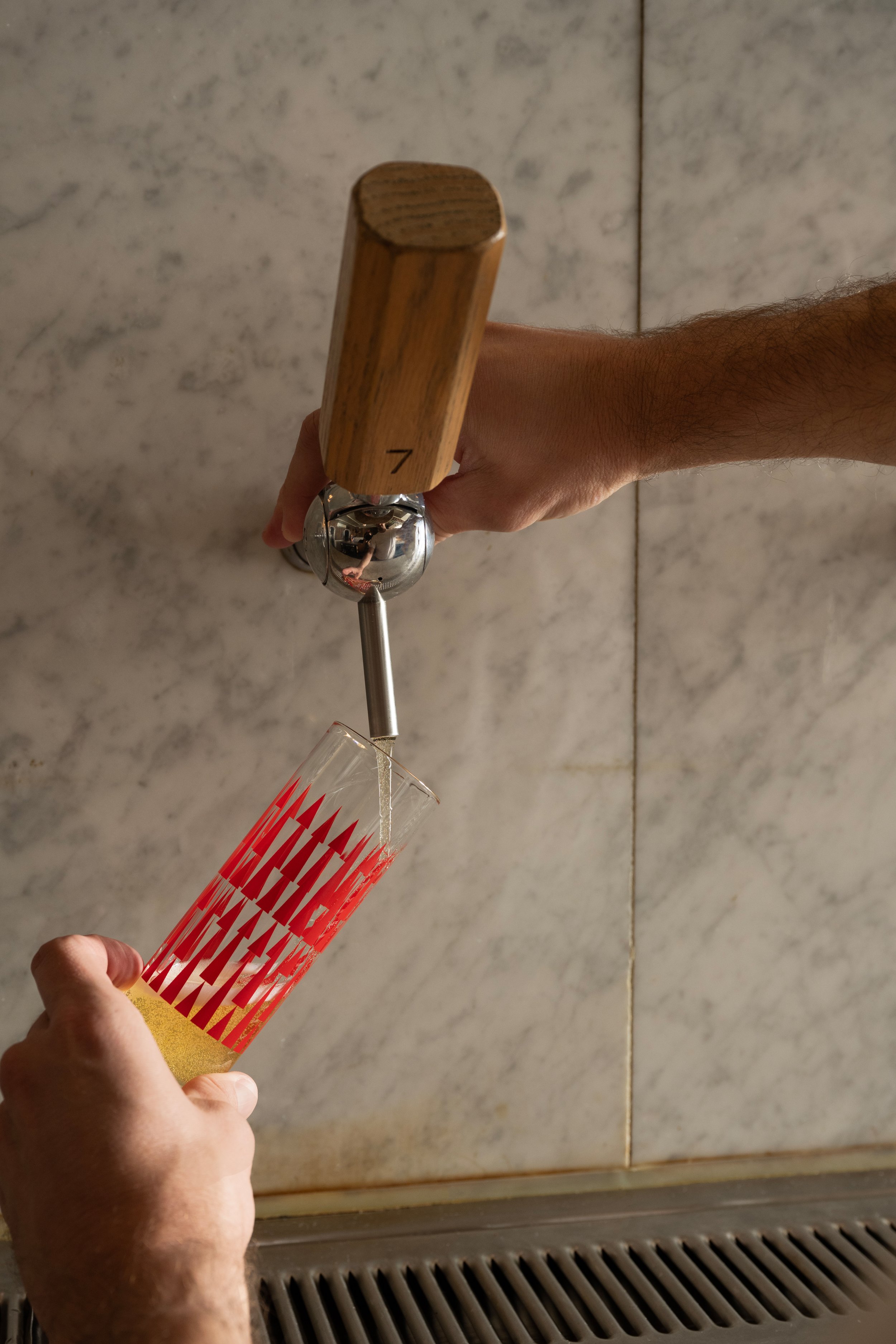 Bartender pouring a golden beer from tap 7 into a red patterned Tørst pilsner glass against a marble bar back