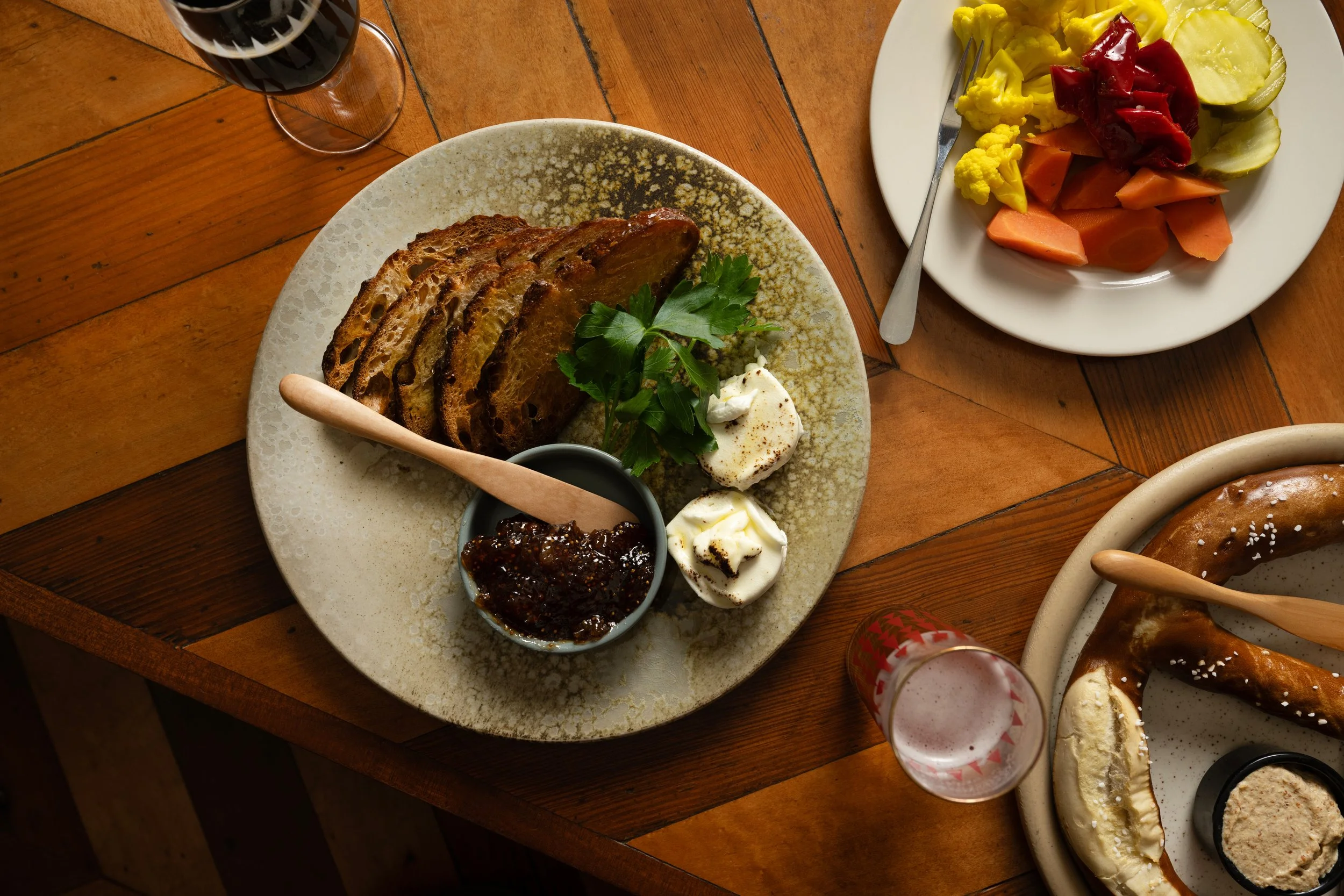 Overhead table spread at Tørst featuring cheese plate, pickled vegetables, and a pretzel alongside beer and patterned glassware