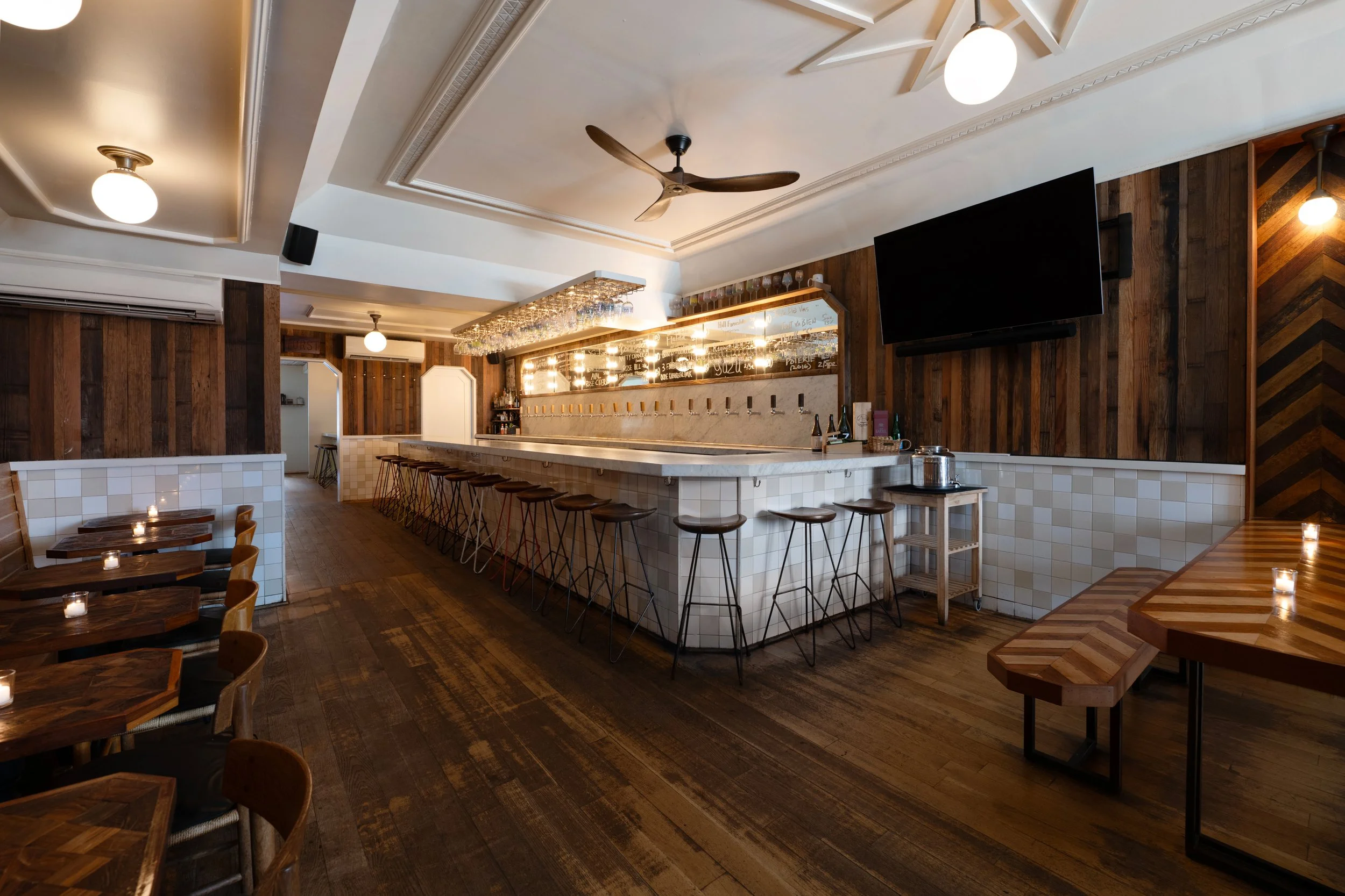 Wide view of Tørst's main bar with marble countertop, draft taps, bar stools, and wood-paneled walls