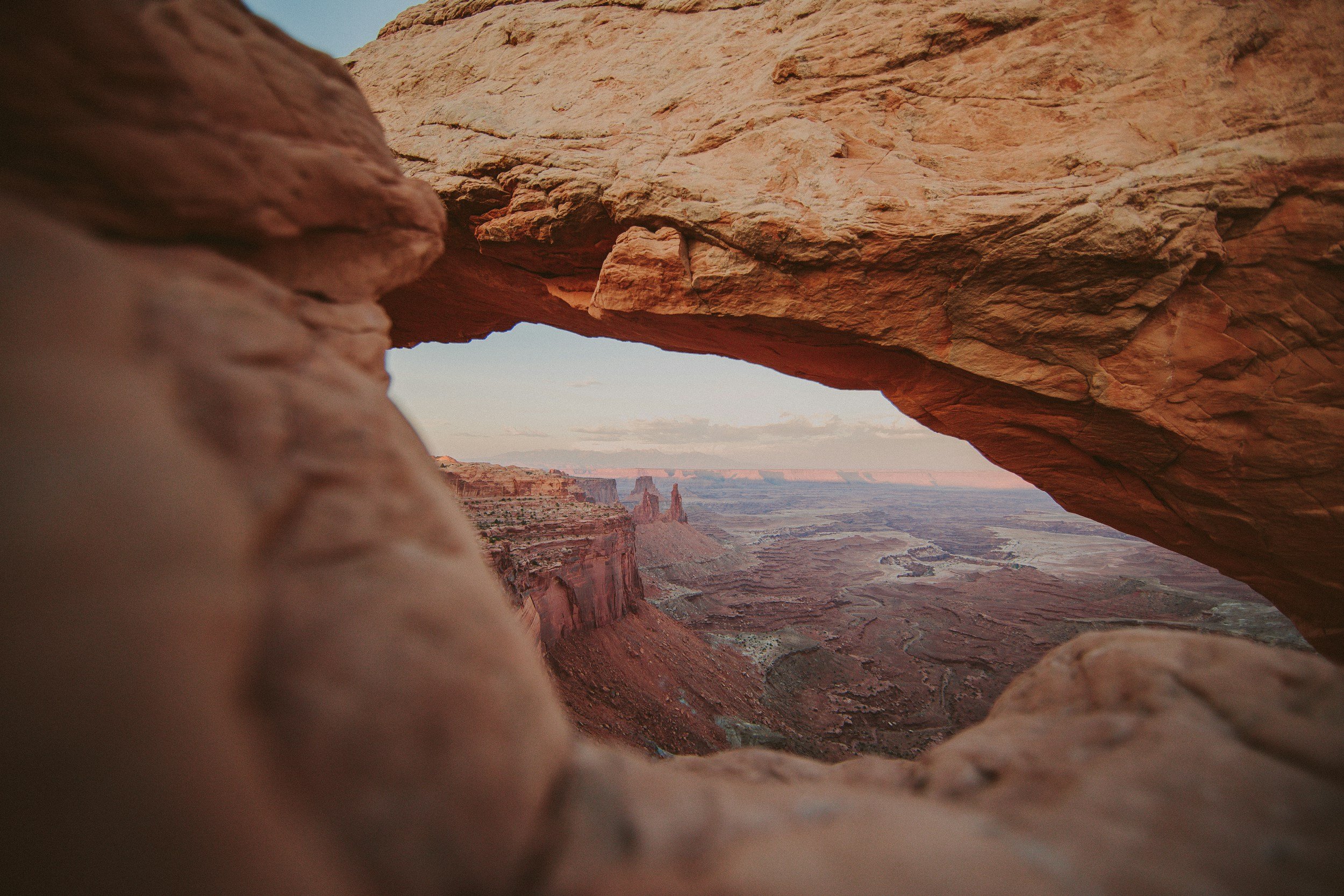 View of Grand Canyon through a rock arch, with rugged red rock formations and a winding river below.