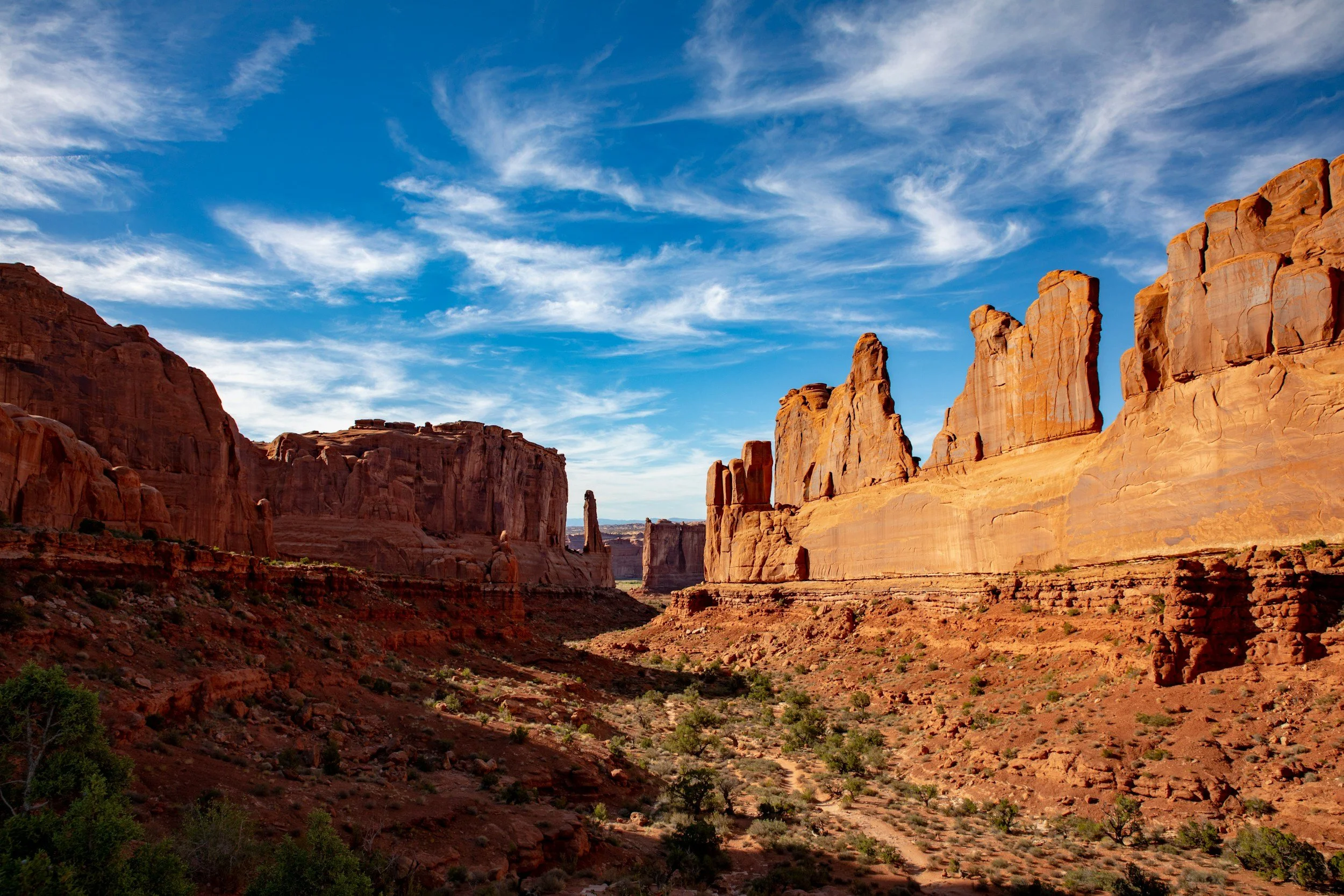 Red sandstone cliffs and formations under a blue sky with scattered clouds, typical of a desert landscape.