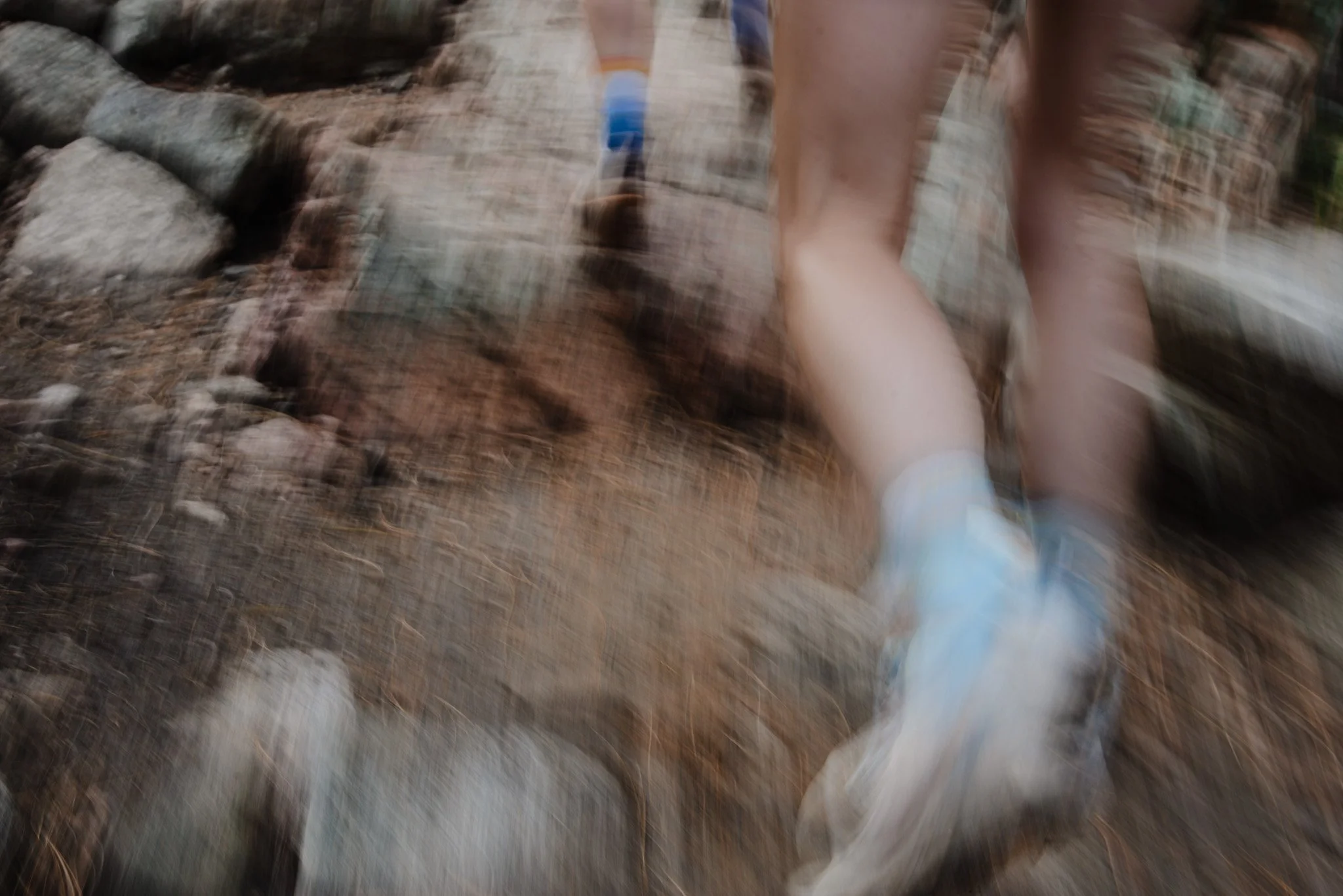 A blurry photo of a person's legs and feet running on a rocky outdoor trail with dirt and small rocks.