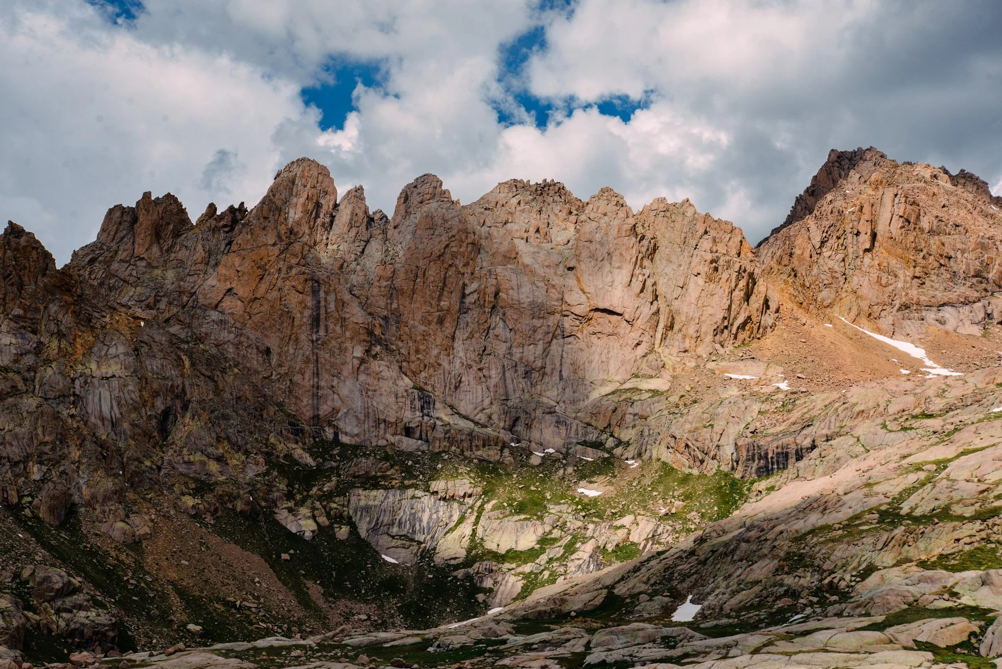 Rocky mountain landscape with rugged cliffs, patches of snow, and a cloudy sky.