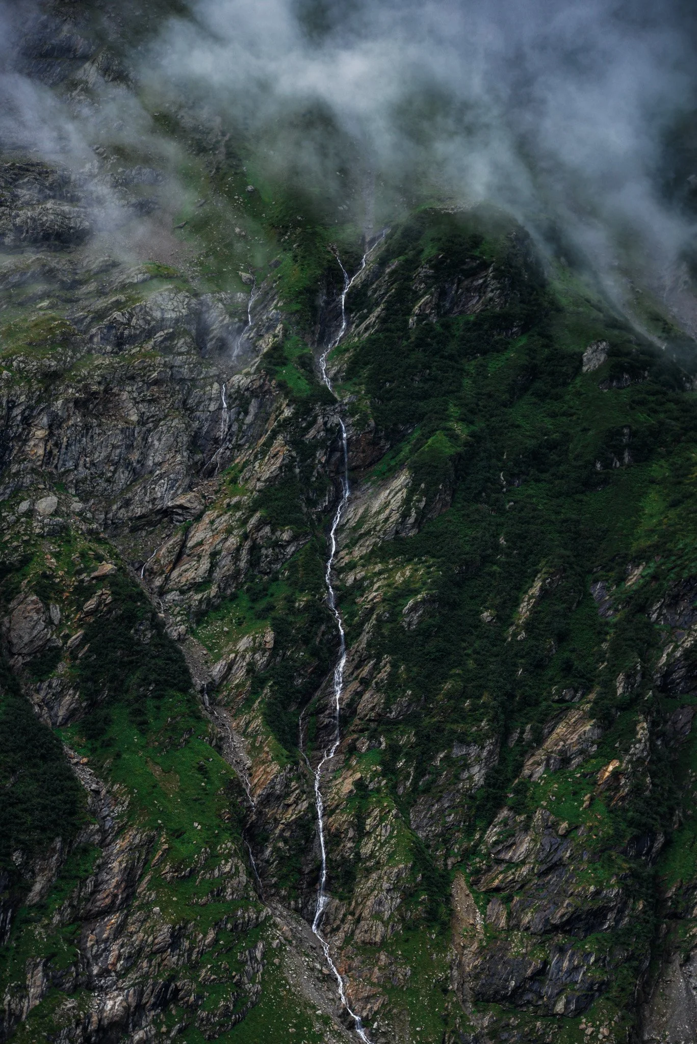 A mountain with green slopes and flowing streams, partially covered by clouds or fog.