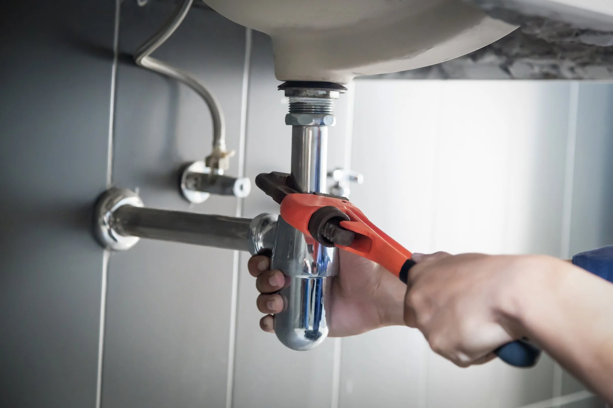 Person using a wrench to tighten or loosen a pipe under a sink in a kitchen.