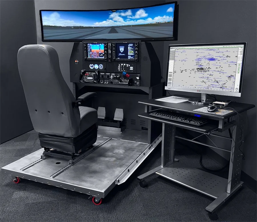 Simulated aircraft cockpit setup with a chair, flight instruments, a large screen display showing a runway view, and a computer with charts for training or testing purposes.