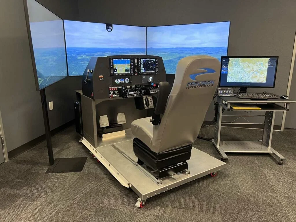 Flight simulator cockpit with multiple screens, a pilot's seat, and flight controls, used for pilot training.