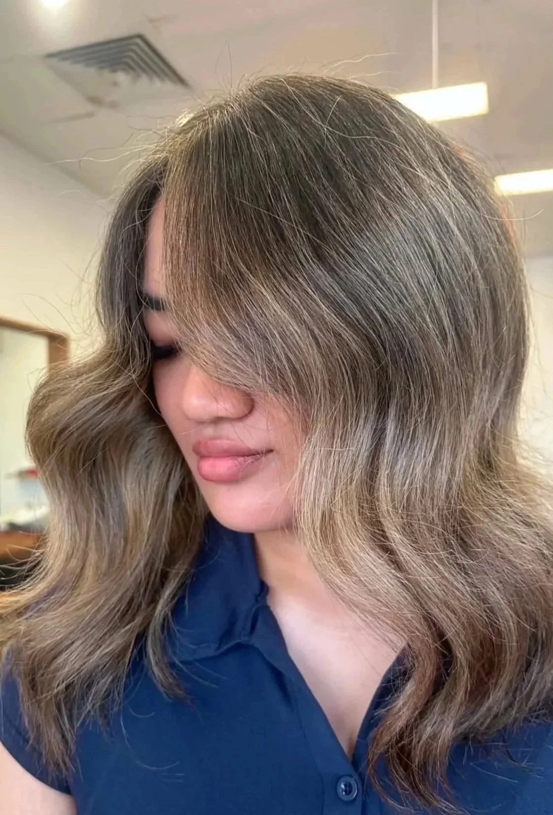 Close-up of a woman with shoulder-length, wavy, silver-blonde hair styled in loose waves, wearing a dark blue top, indoors.