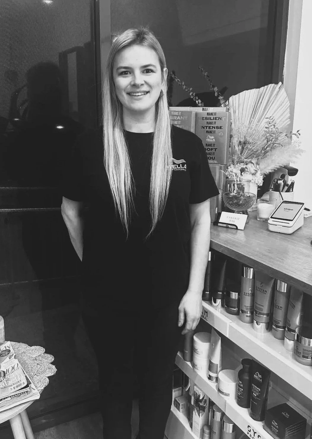 A smiling woman with long hair standing in a store behind a display of skincare products.