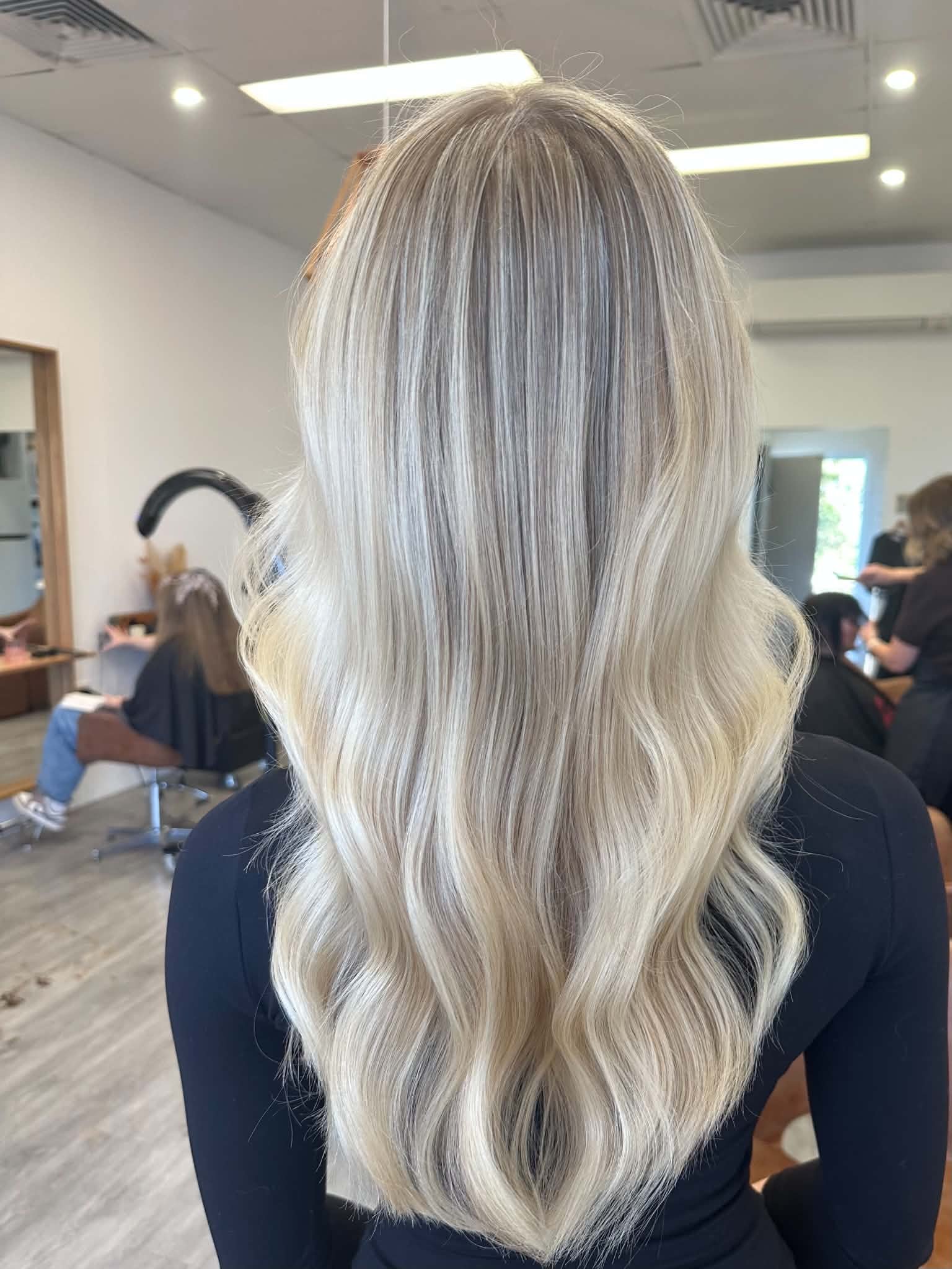 Back of a person's head with long, blond, wavy hair in a hair salon.
