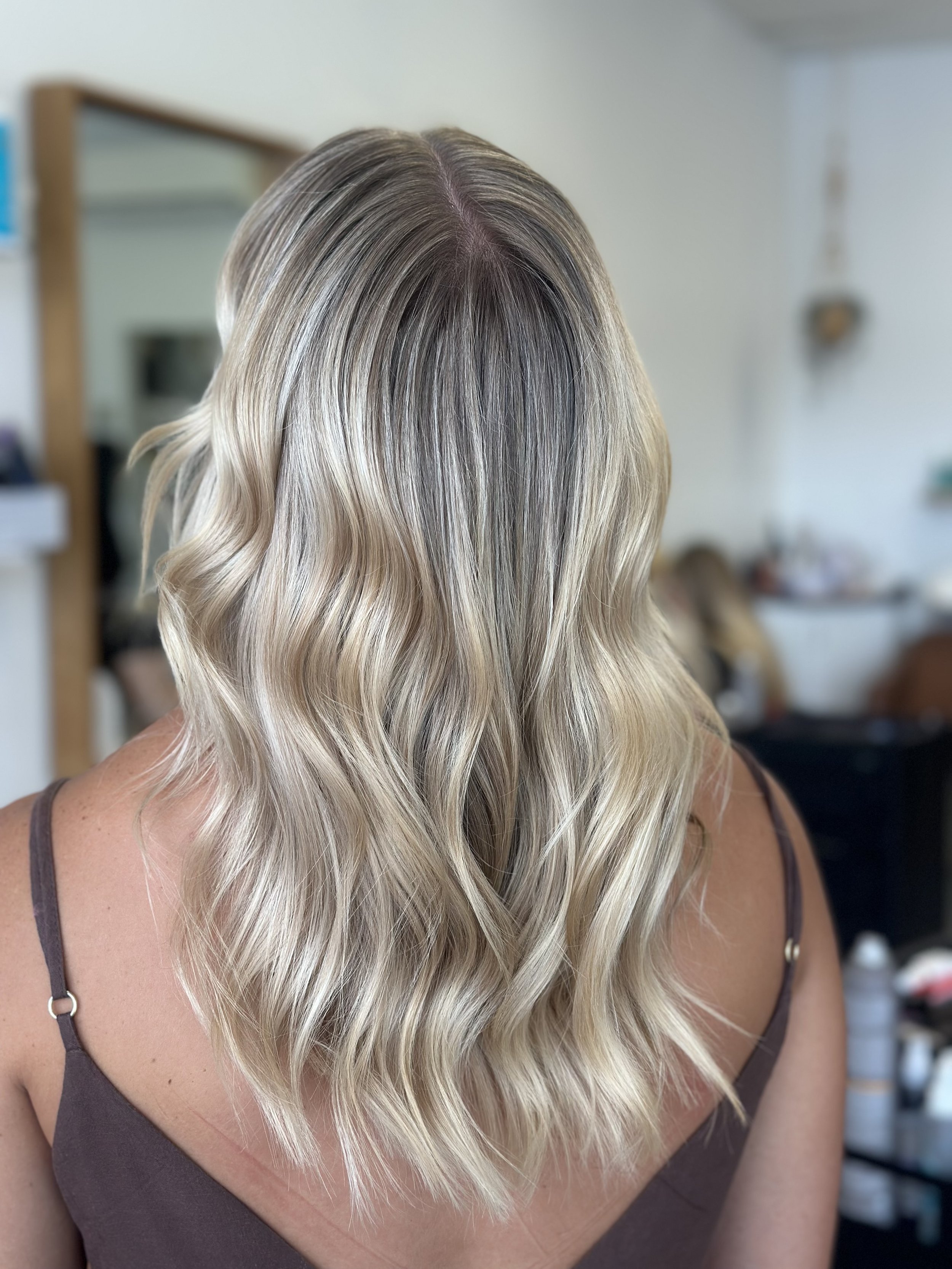 Woman with blonde, wavy hair in loose curls wearing a brown tank top.
