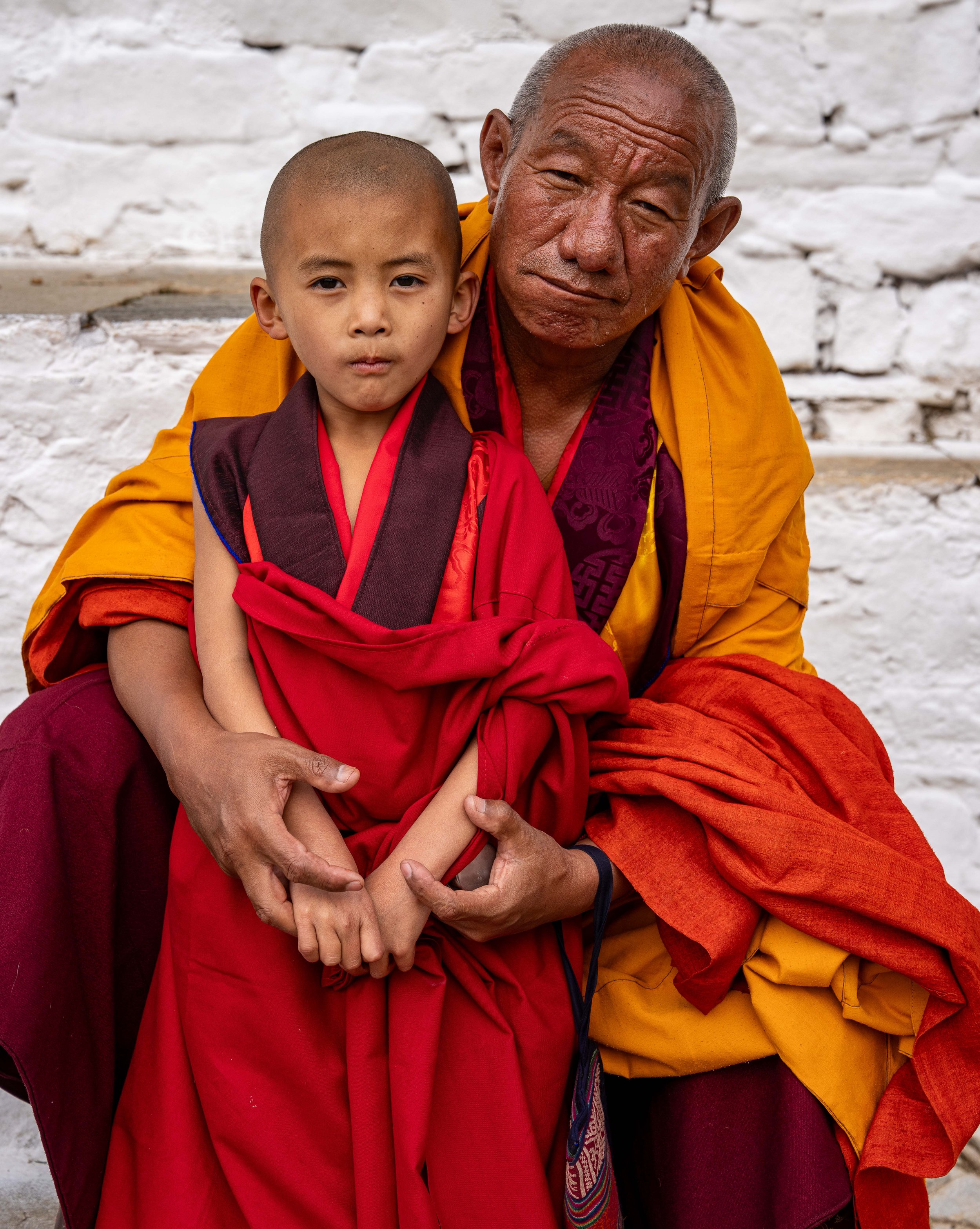 A young monk and an older monk sitting together, wearing traditional robes, in Gasa Bhutan