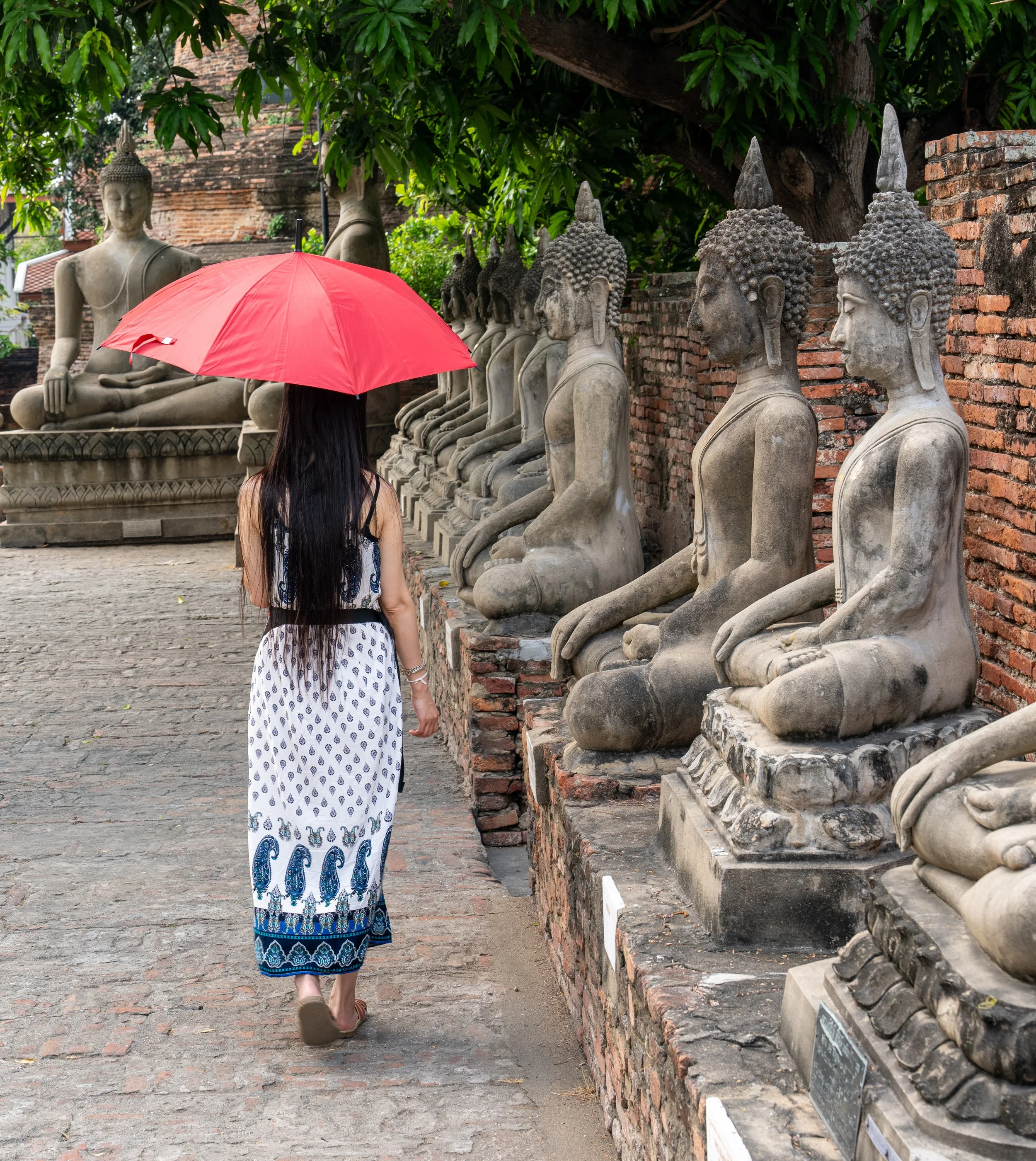 A woman walks past a row of Buddhas in Thailand