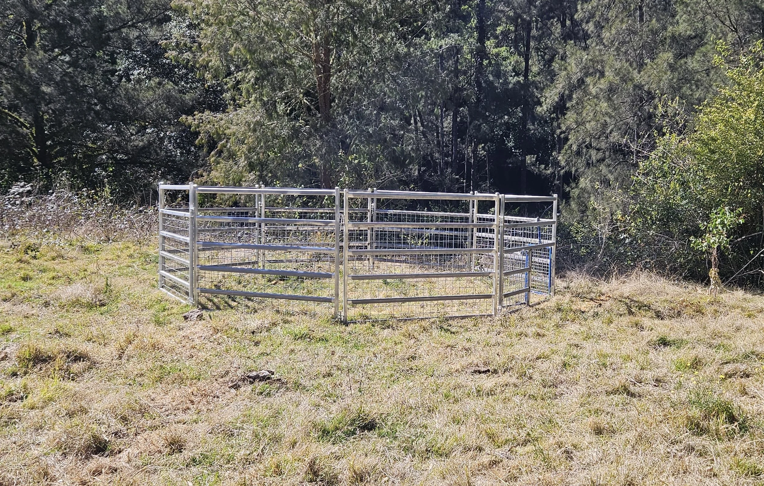 Metal livestock pen or cage on grassy area with trees in the background.