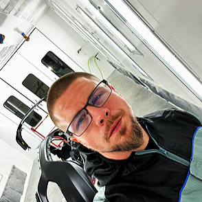 Close-up of a man with glasses and a beard, taking a selfie in a store aisle with electronics and speakers.